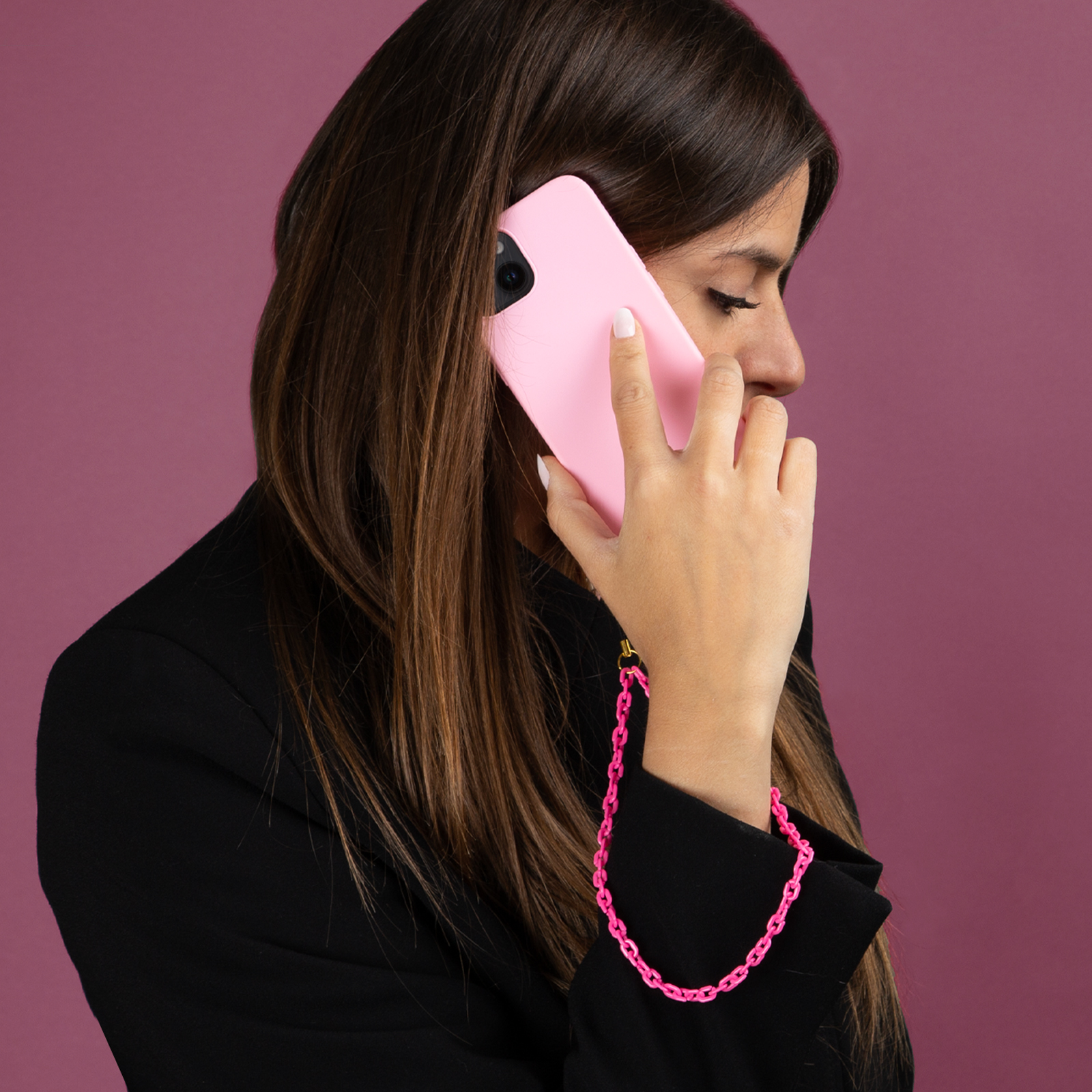 Mujer con pelo castaño hablando por teléfono con un móvil rosa, vistiendo chaqueta negra.