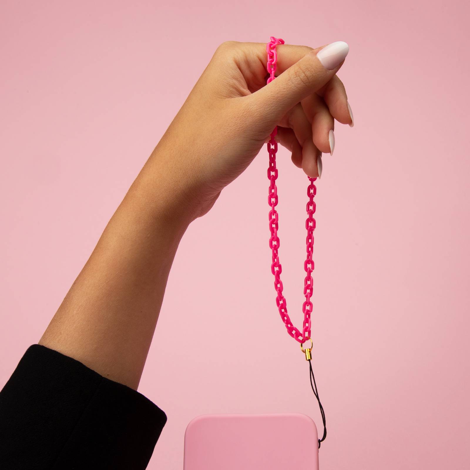 Una mano sostiene un cordón de cadena rosa neón sobre un teléfono rosa.
