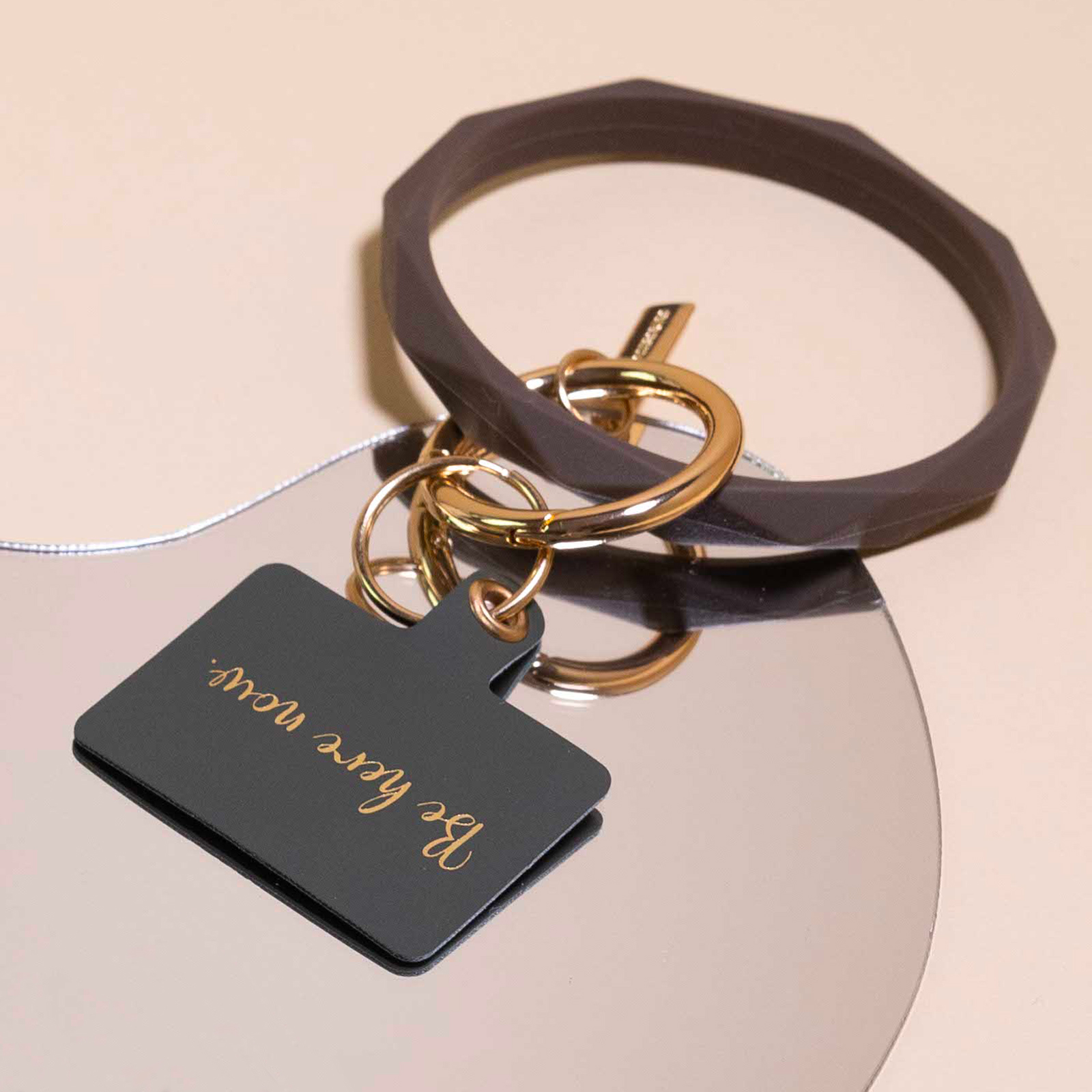 Un'etichetta grigio scuro con testo dorato 'Be here now' su uno specchio.