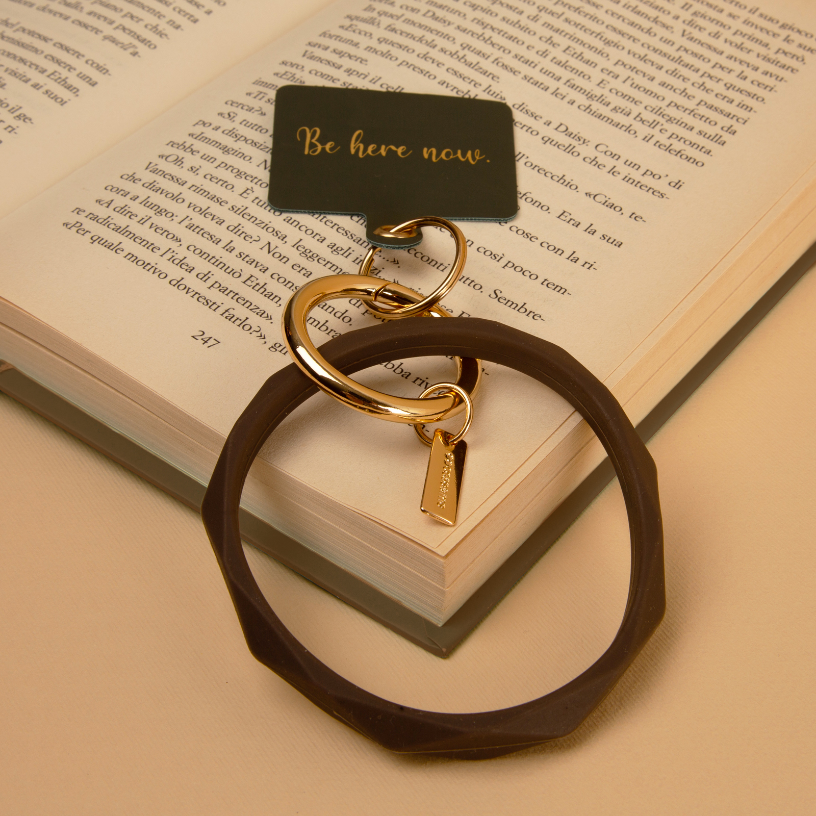 Un libro aperto con un biglietto verde scuro "Be here now". Un portachiavi accanto.