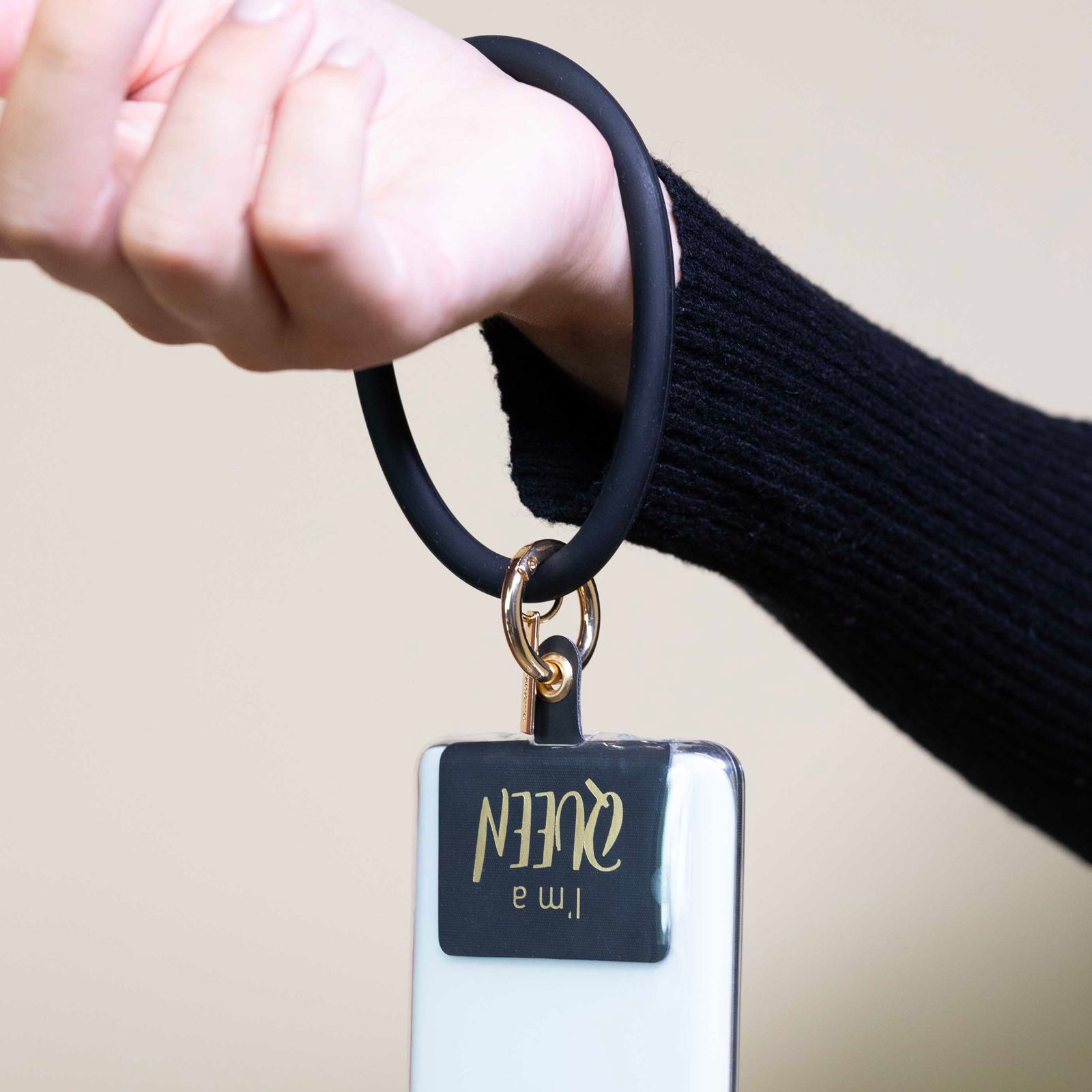 Una mano con suéter negro lleva un brazalete con un dije.