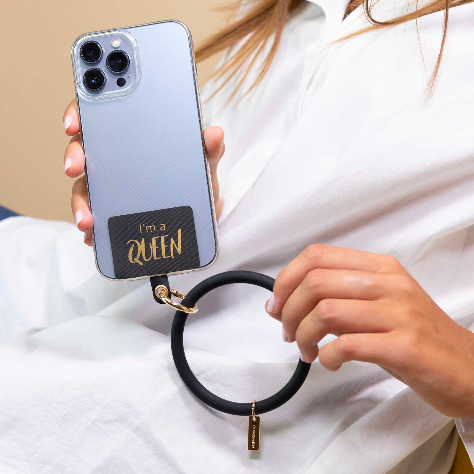 Una persona sostiene un smartphone azul claro con una pulsera negra que dice "I'm a QUEEN".