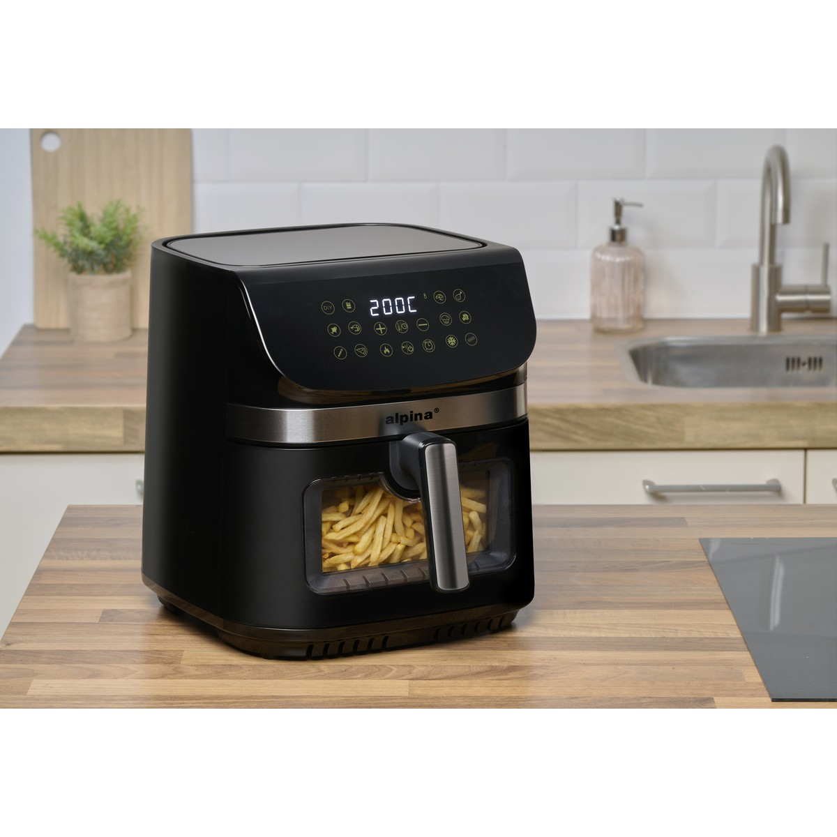 Black air fryer with french fries in window, on a wooden counter.