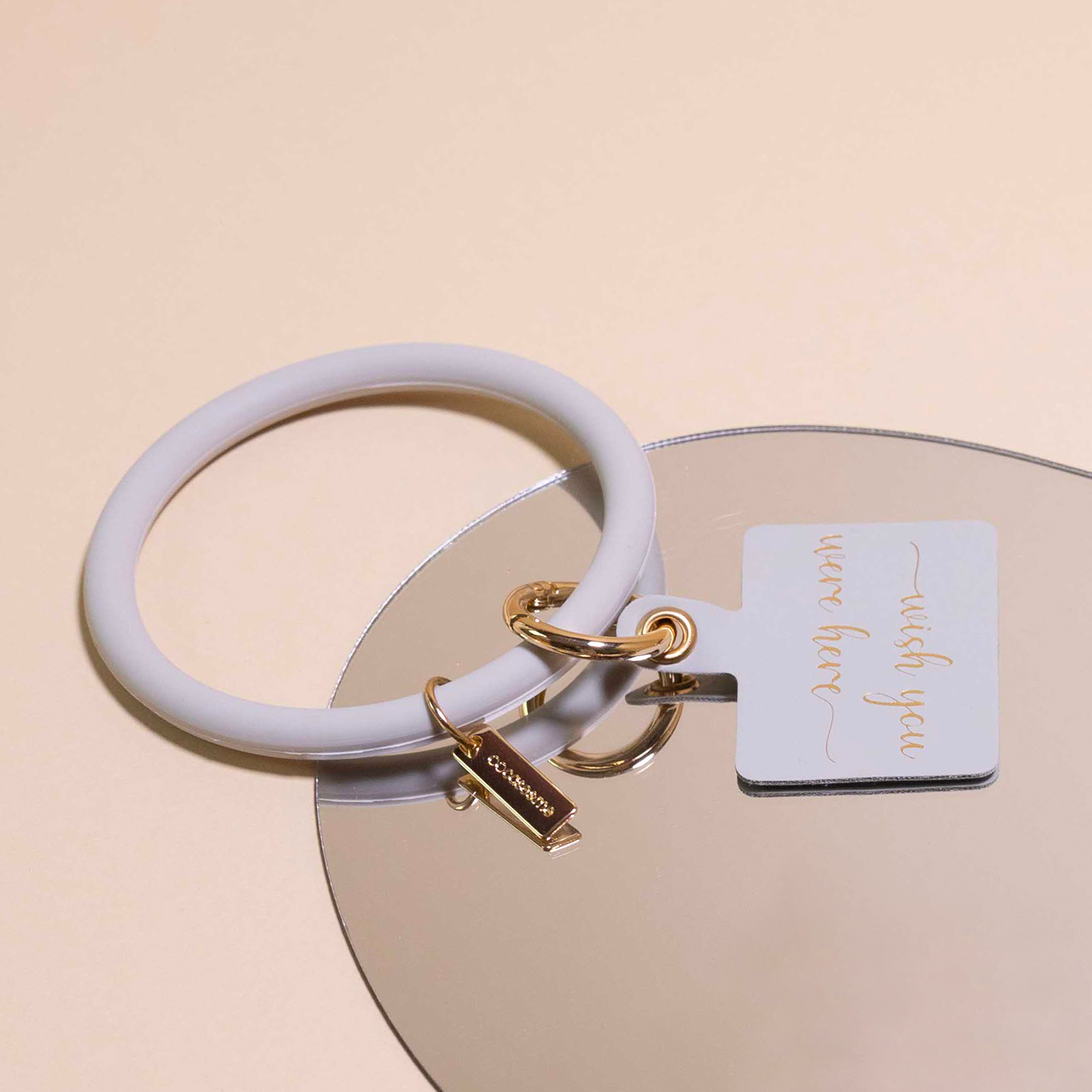 Un llavero de pulsera gris claro con herrajes dorados y una etiqueta.