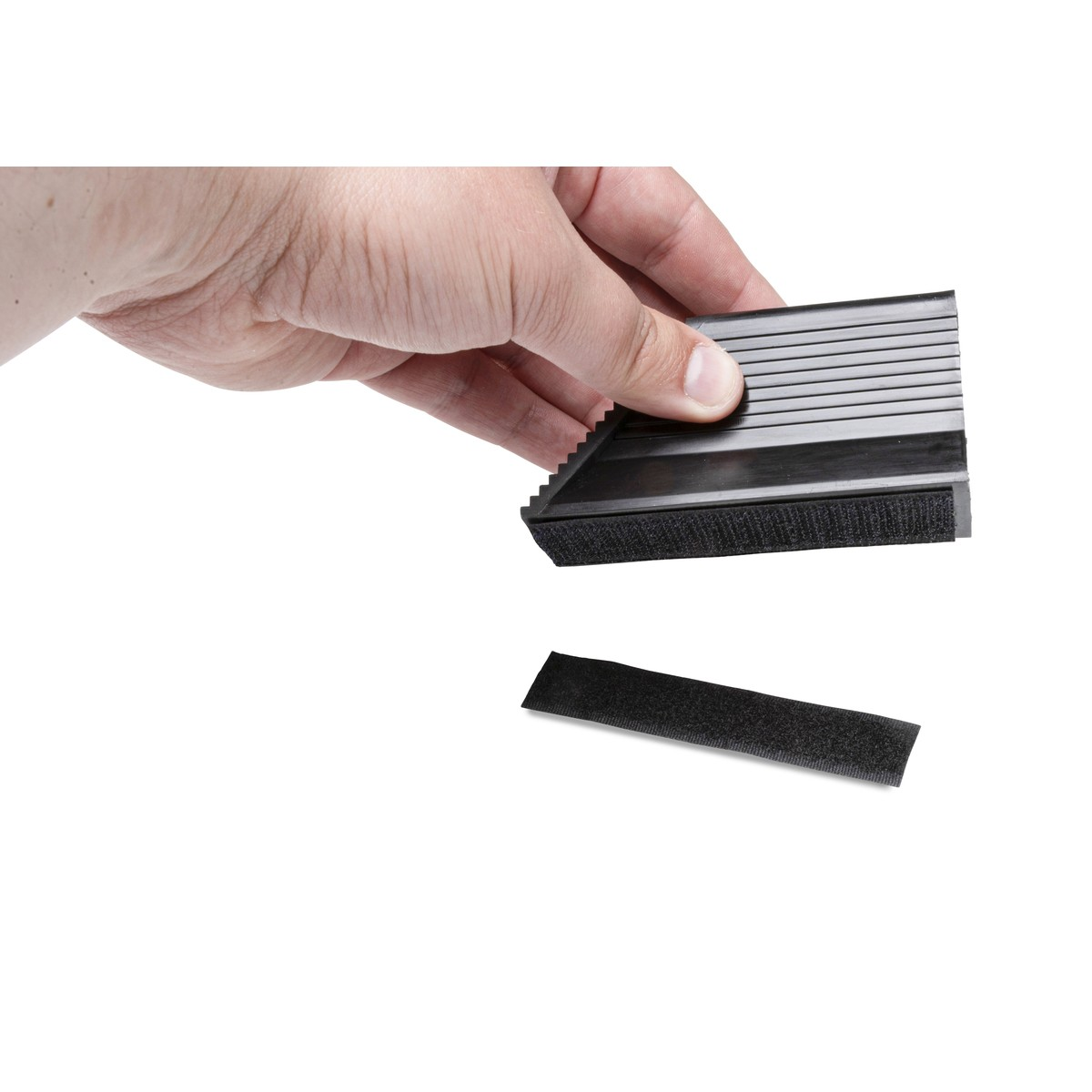 A hand holds a black wedge with velcro. A velcro strip lies below it.