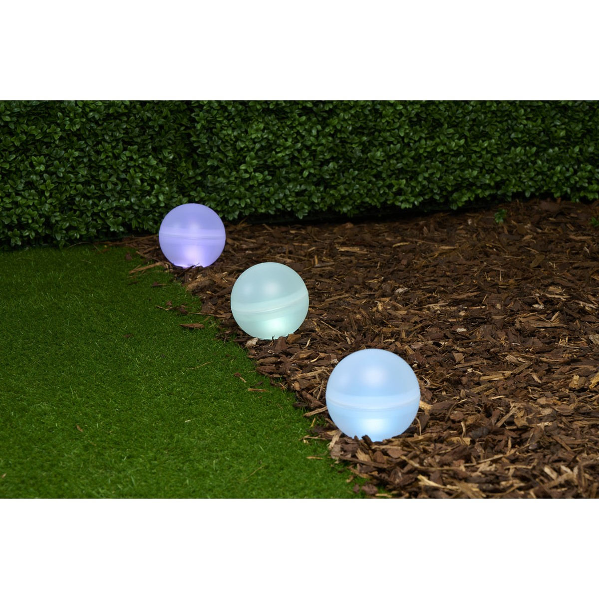 Three glowing orbs on grass and mulch next to a hedge.