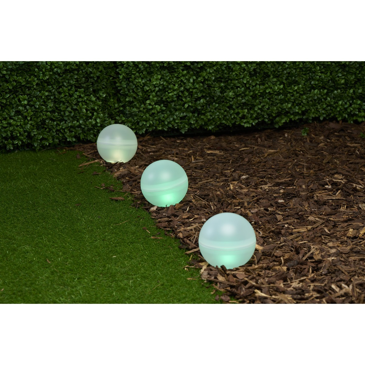 Three glowing orbs on grass and mulch next to a hedge.