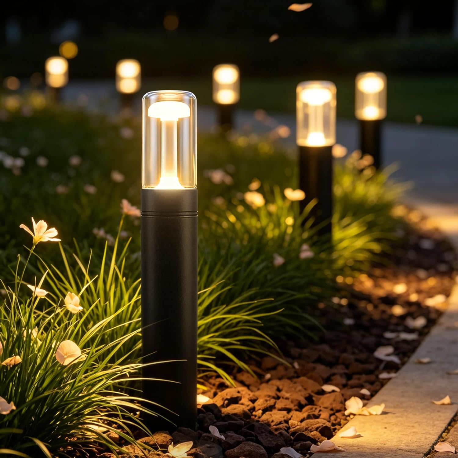 Moderne schwarze Pollerleuchten beleuchten nachts einen Gartenweg mit Gras und Blumen.