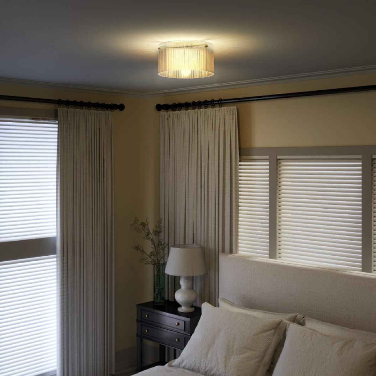 Ein Schlafzimmer mit Nachttisch, Lampe, Vorhängen, Jalousien und Deckenleuchte.