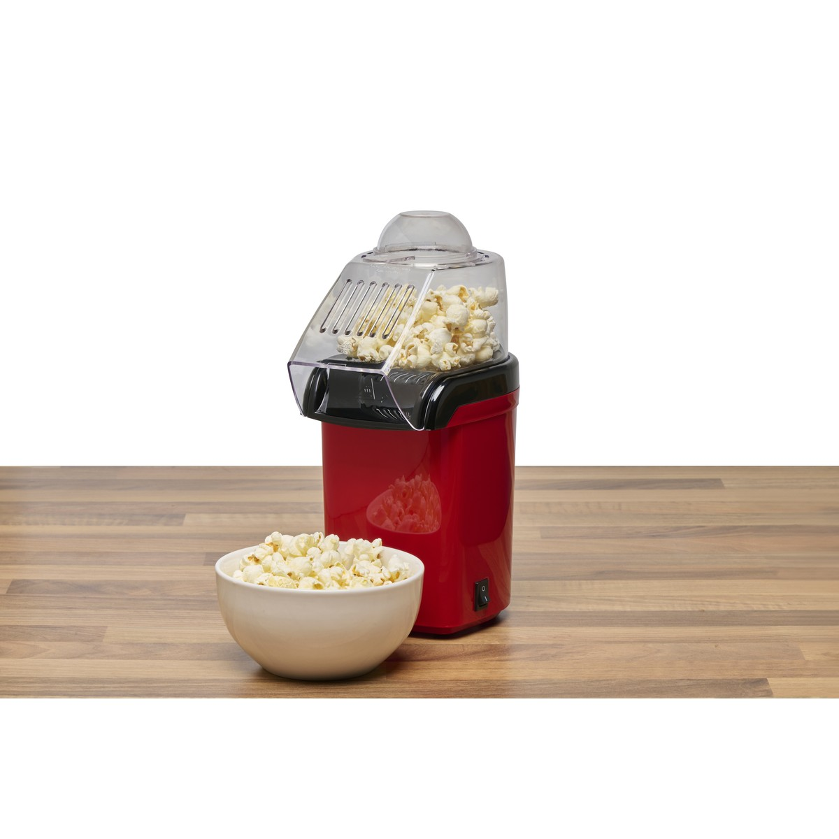 Red popcorn maker with a bowl of popcorn on a wooden table.