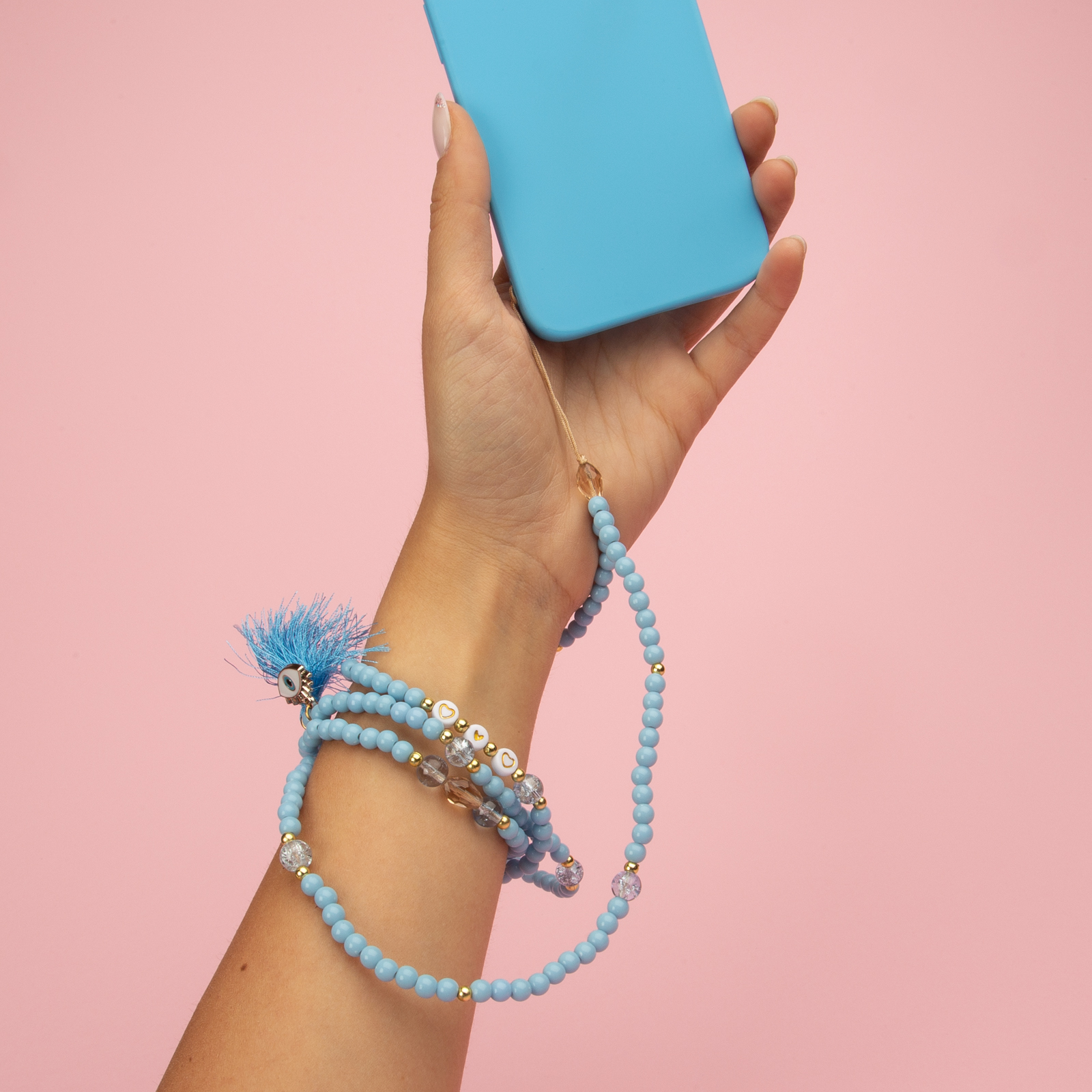 Una mano sujeta un teléfono azul con una cadena de perlas y un dije de borla.