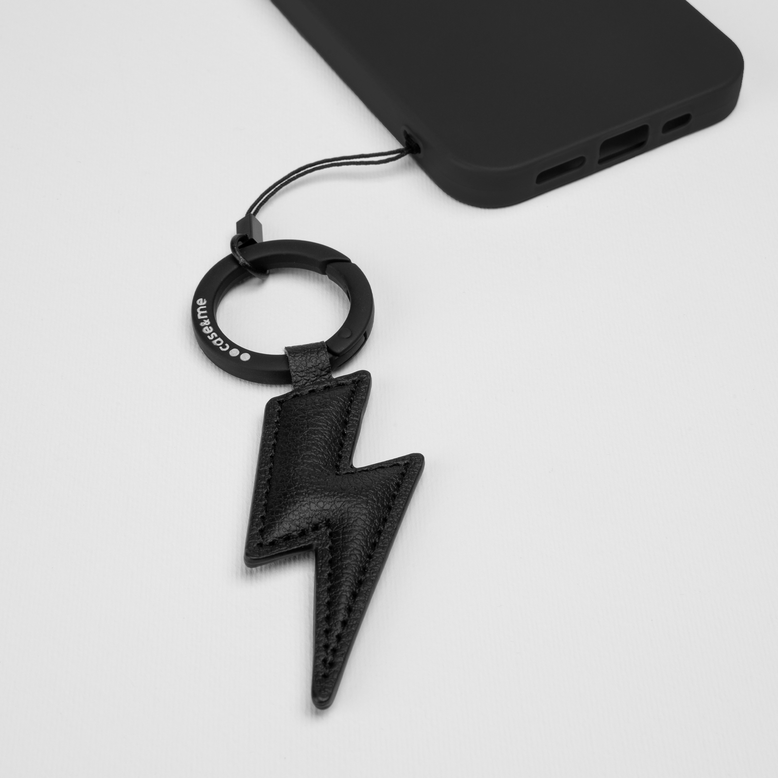 Colgante de rayo negro con anilla unido a una funda de teléfono negra.