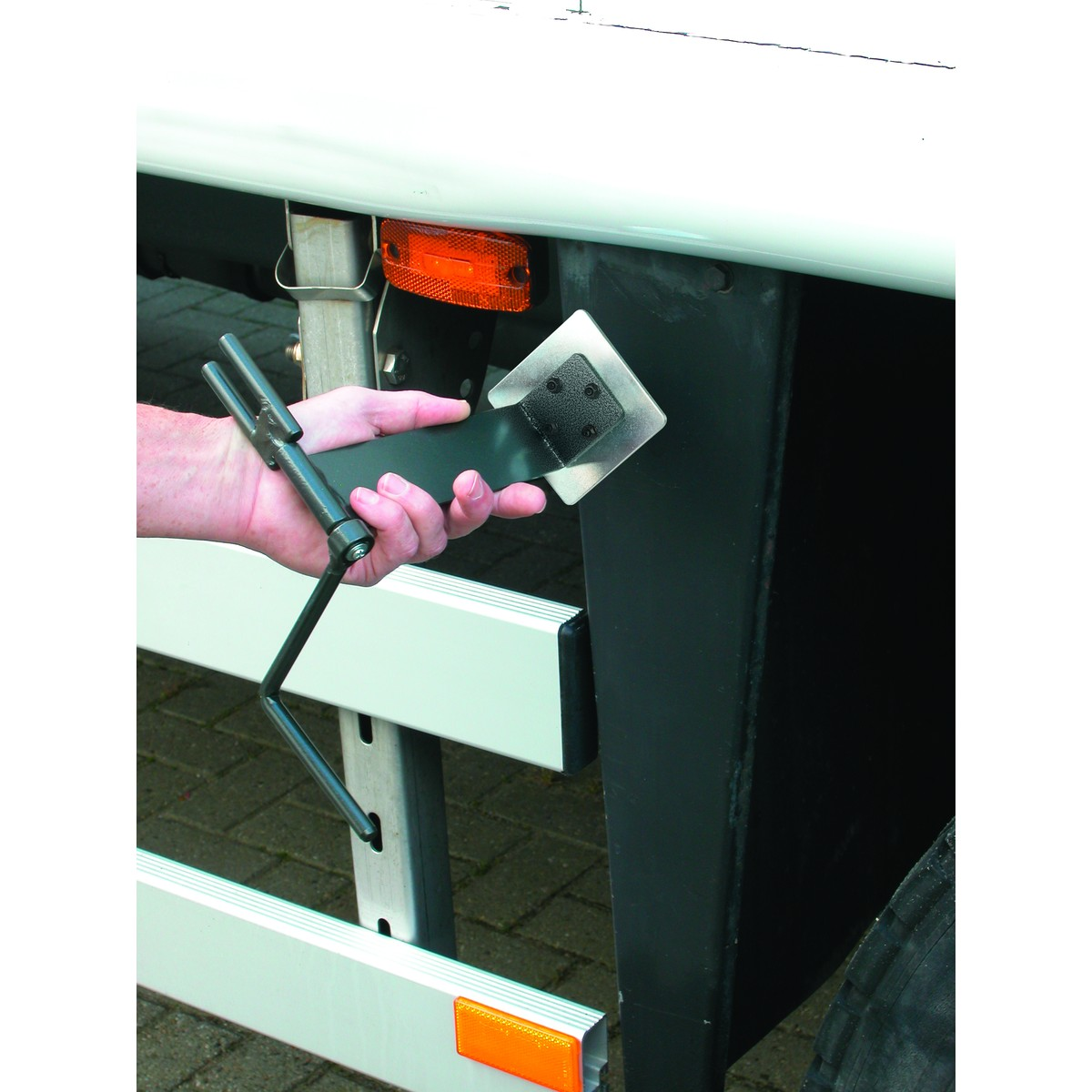 Een hand houdt een gereedschap met een zwengel en een vierkante kop vast bij een vrachtwagen.