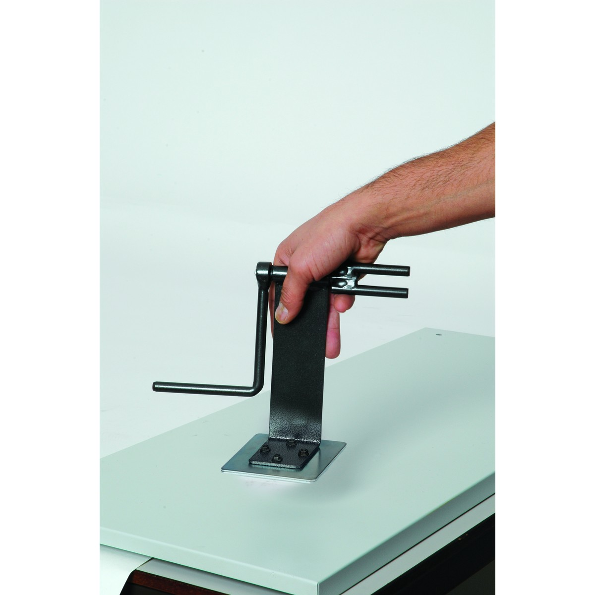 Een hand houdt een zwengel vast op een metalen gereedschap gemonteerd op een bureau.