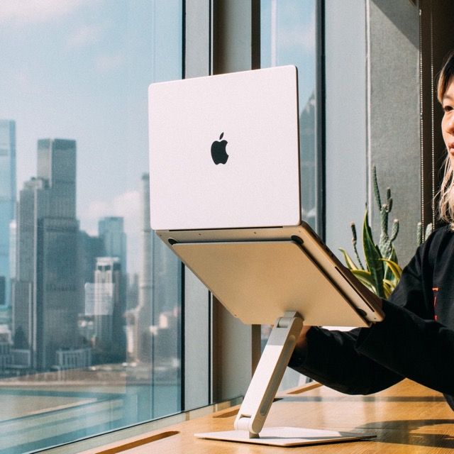 Una donna con un laptop su un supporto davanti a una finestra con vista sulla città.