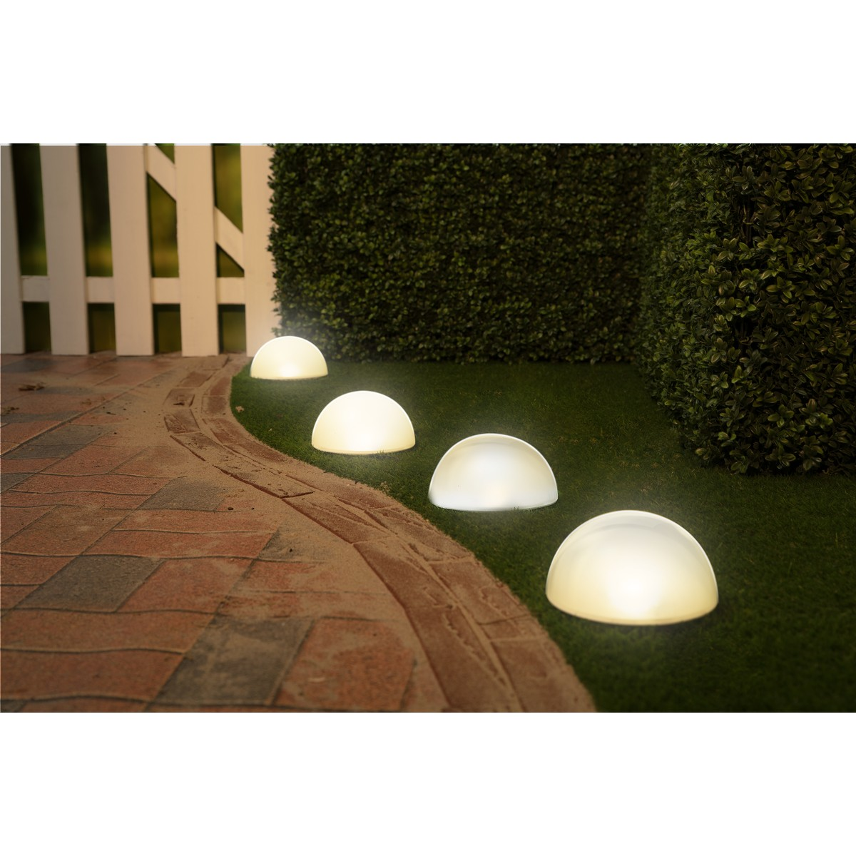 Four glowing half-dome lights line a path next to a green hedge.