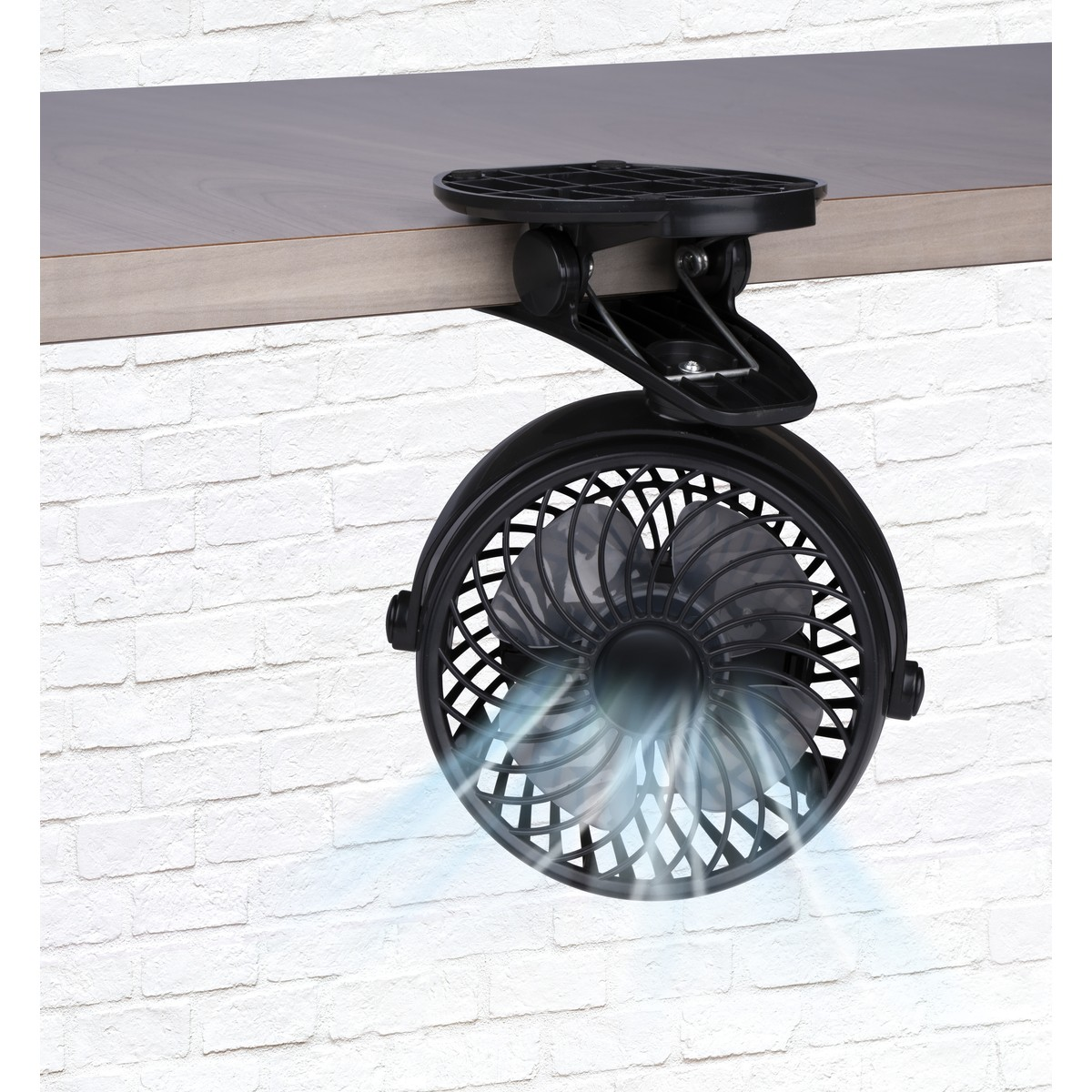 Ein schwarzer Klemmventilator mit sich drehenden Rotorblättern, der Luft auf eine weiße Ziegelwand bläst.