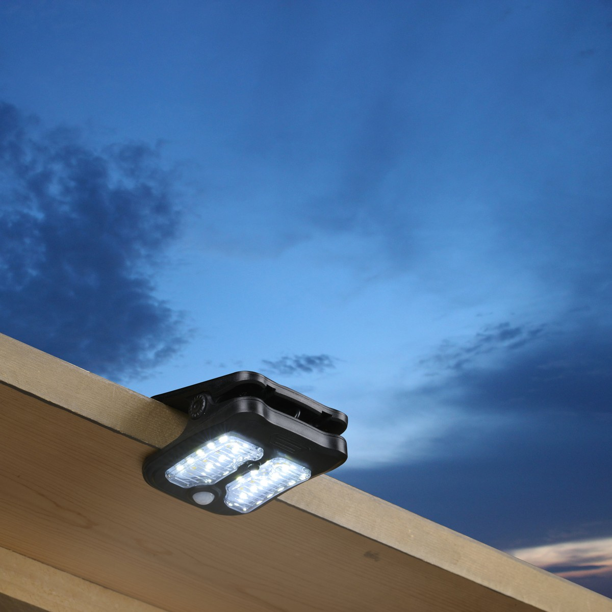 Solar light with motion sensor attached to a wooden beam under a blue sky.