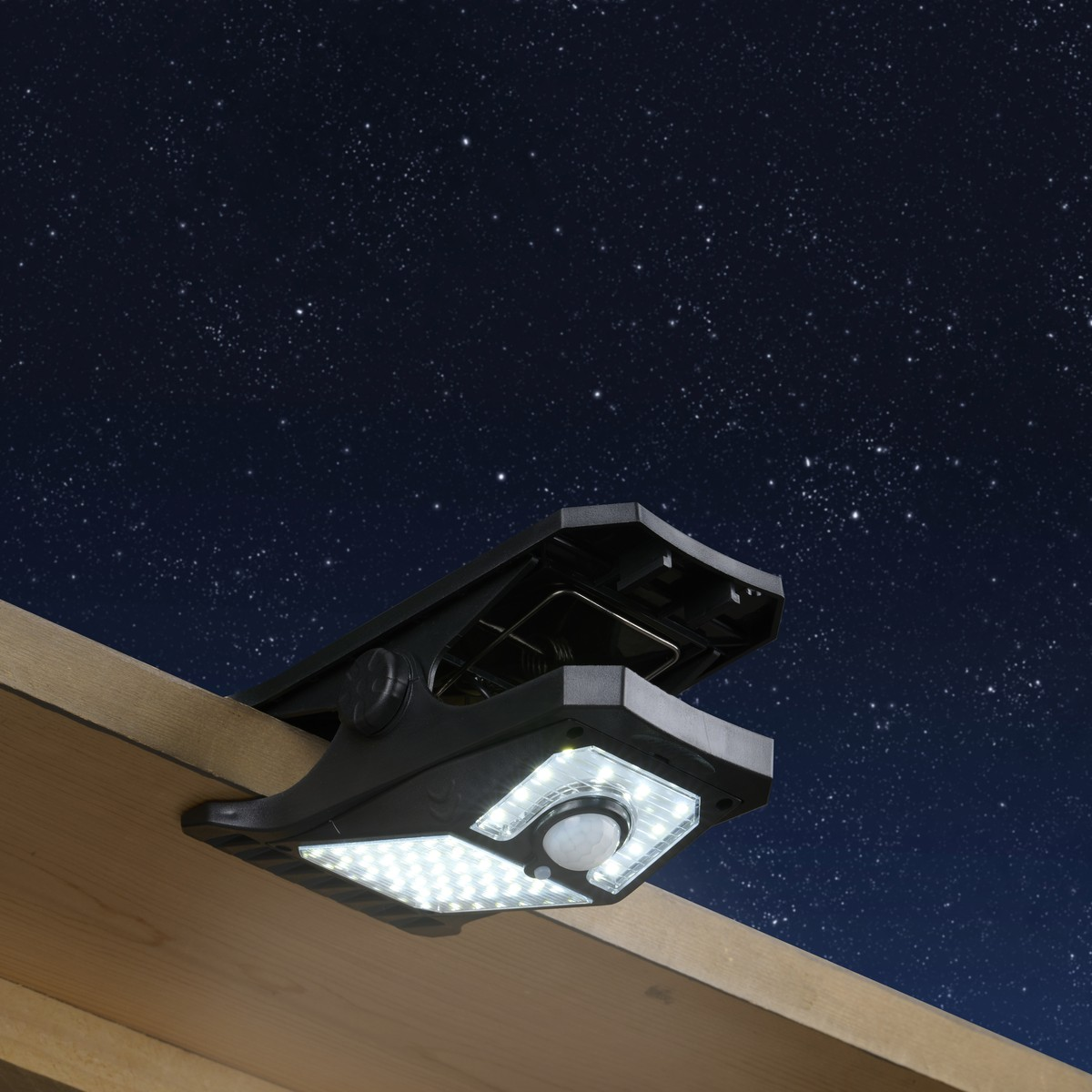 A black solar clip-on spotlight with LEDs and motion sensor is attached to a wooden board.