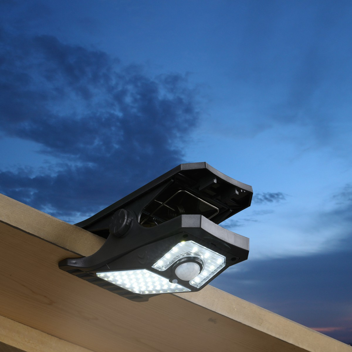 A black solar outdoor light with motion sensor is clipped onto a wooden beam.