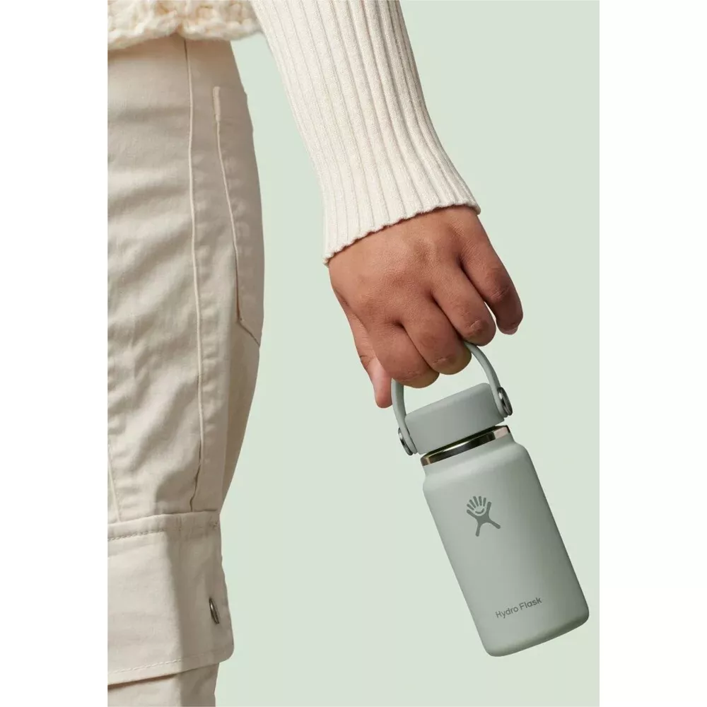 Eine Hand hält eine hellgrüne Hydro Flask Wasserflasche mit Griff.