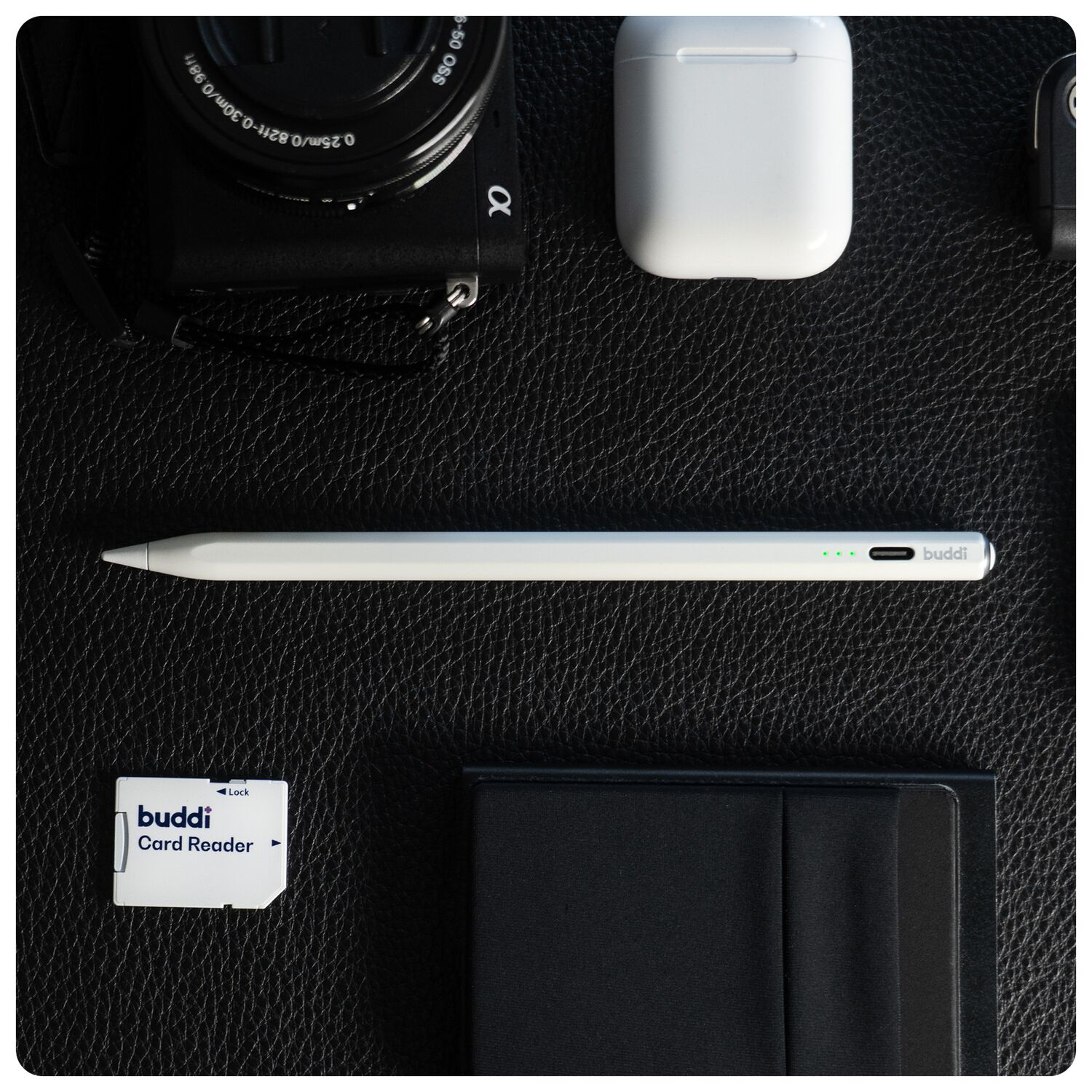 Camera, stylus, oordopjes, kaartlezer en notitieboek op zwart leer.