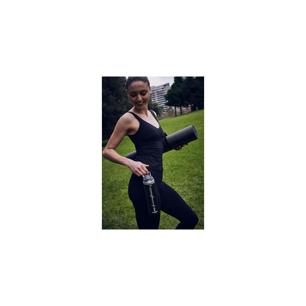Frau in schwarzer Sportkleidung hält Yogamatte und Wasserflasche im Park.