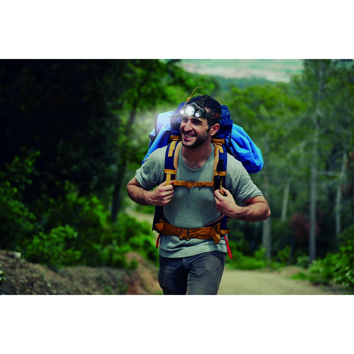 A man with a headlamp and backpack hikes on a forest path.