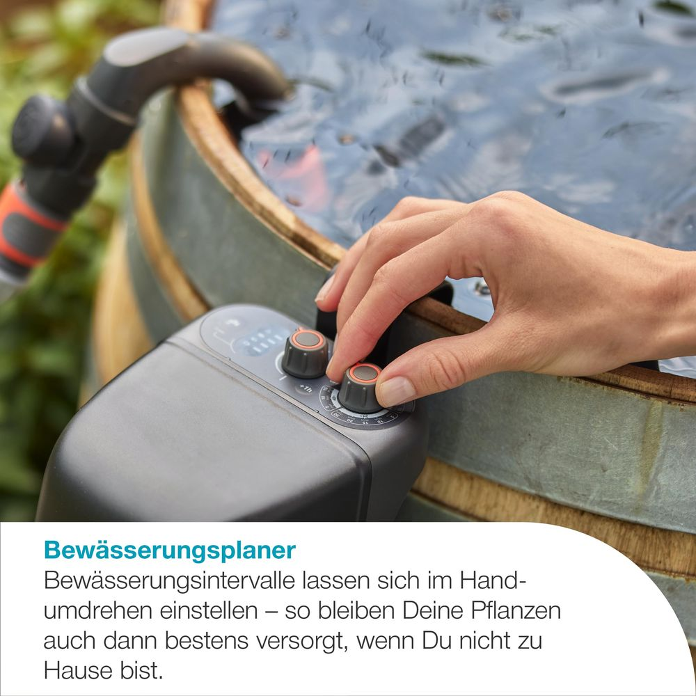 Eine Hand stellt einen Bewässerungsplaner ein, der an einem Holzfass mit Wasser befestigt ist.