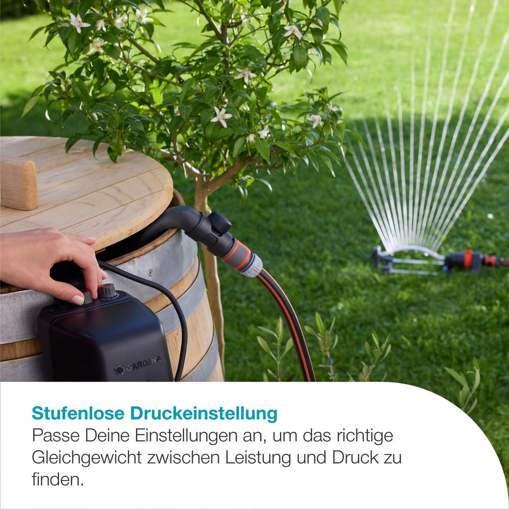 Hand passt schwarzen Regler an Holzfass an, Sprinkler wässert Rasen.