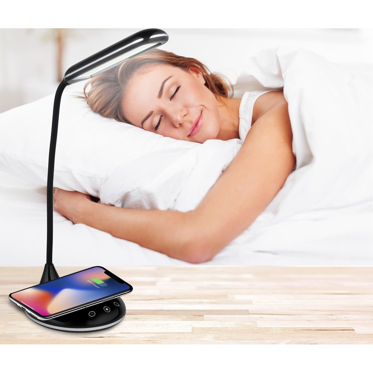 A woman sleeps in bed, a bedside lamp with a phone charging beside it.