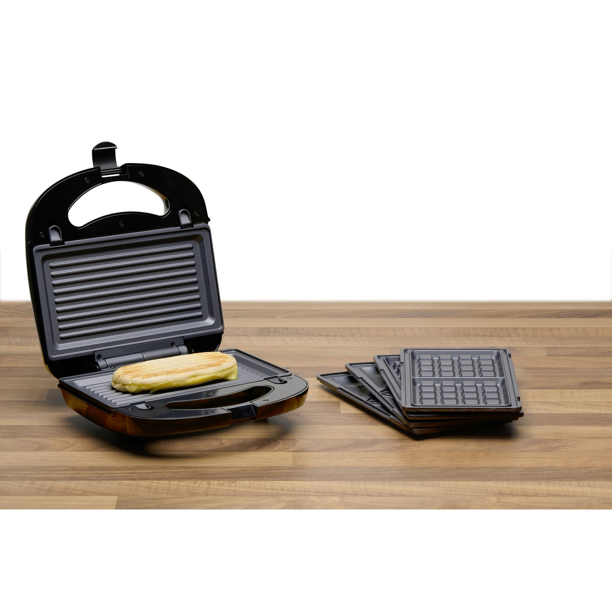 Ein offener Sandwichmaker mit einem Sandwich und austauschbaren Platten daneben.
