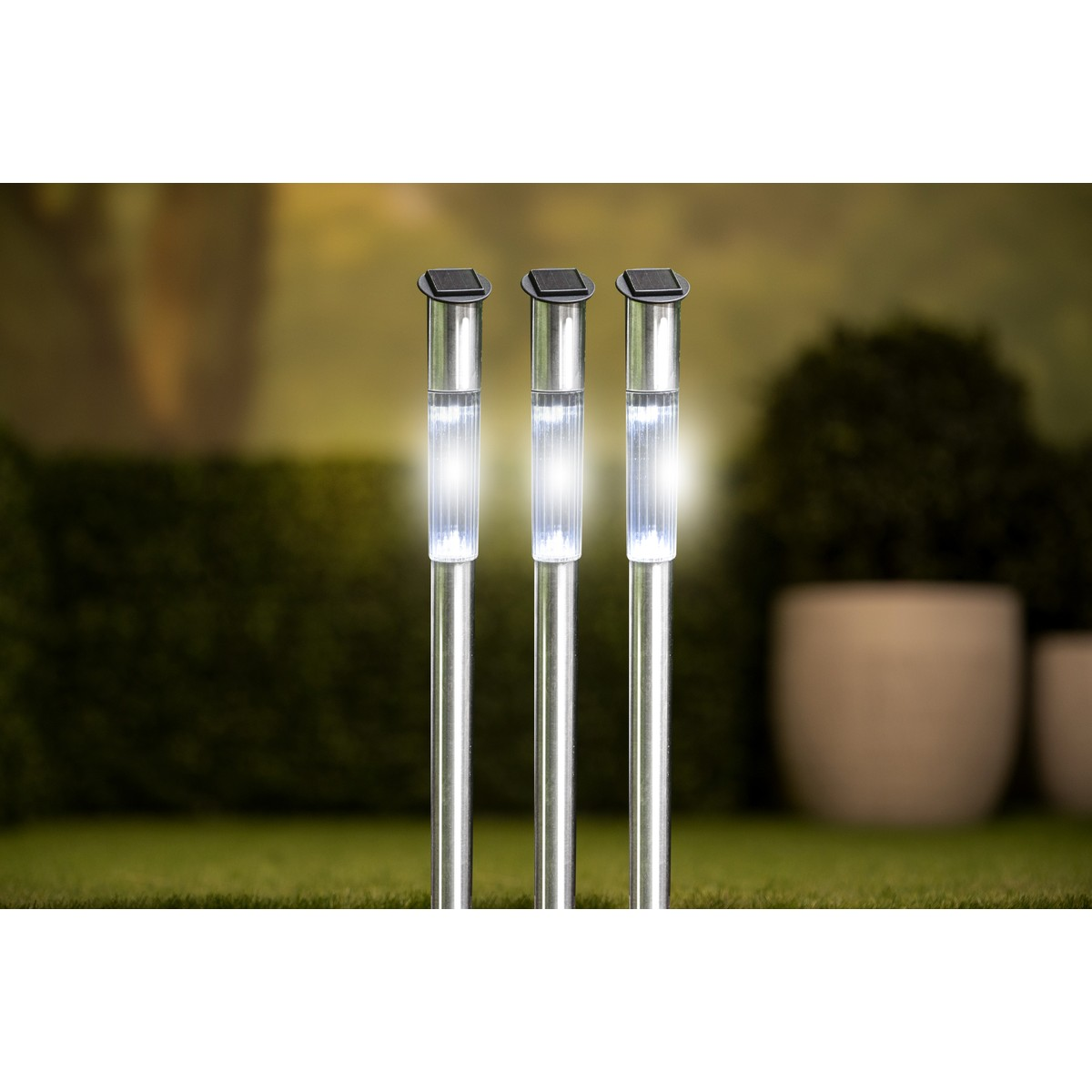 Drei Solarleuchten mit silbernen Stielen und weißen Lichtern auf Rasen.