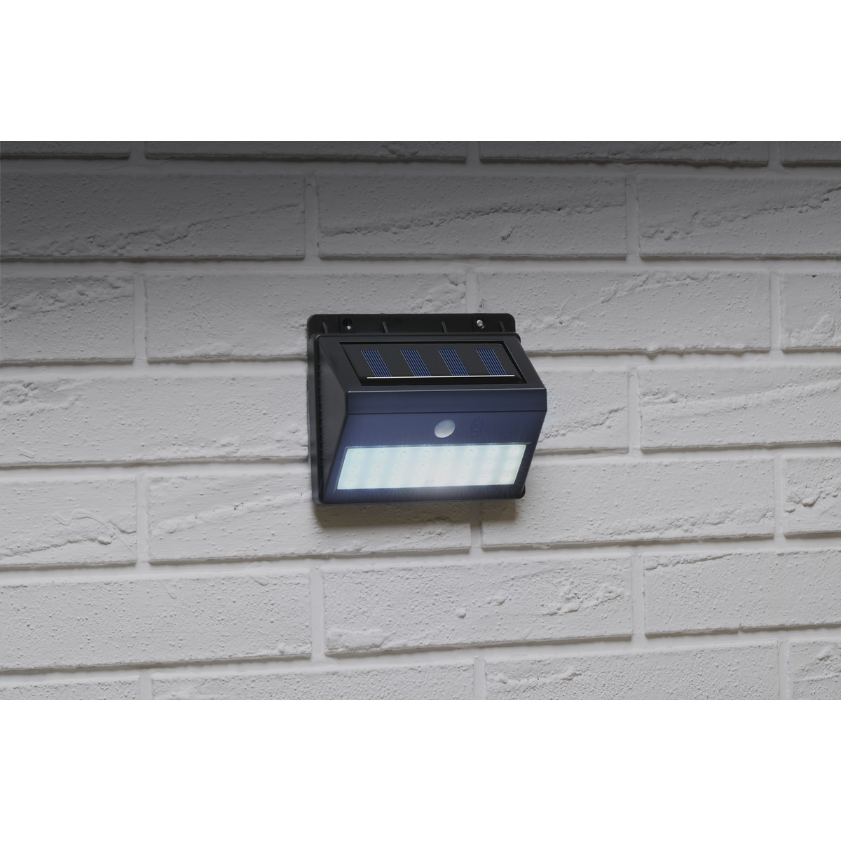 Black solar light with motion sensor mounted on white brick wall.