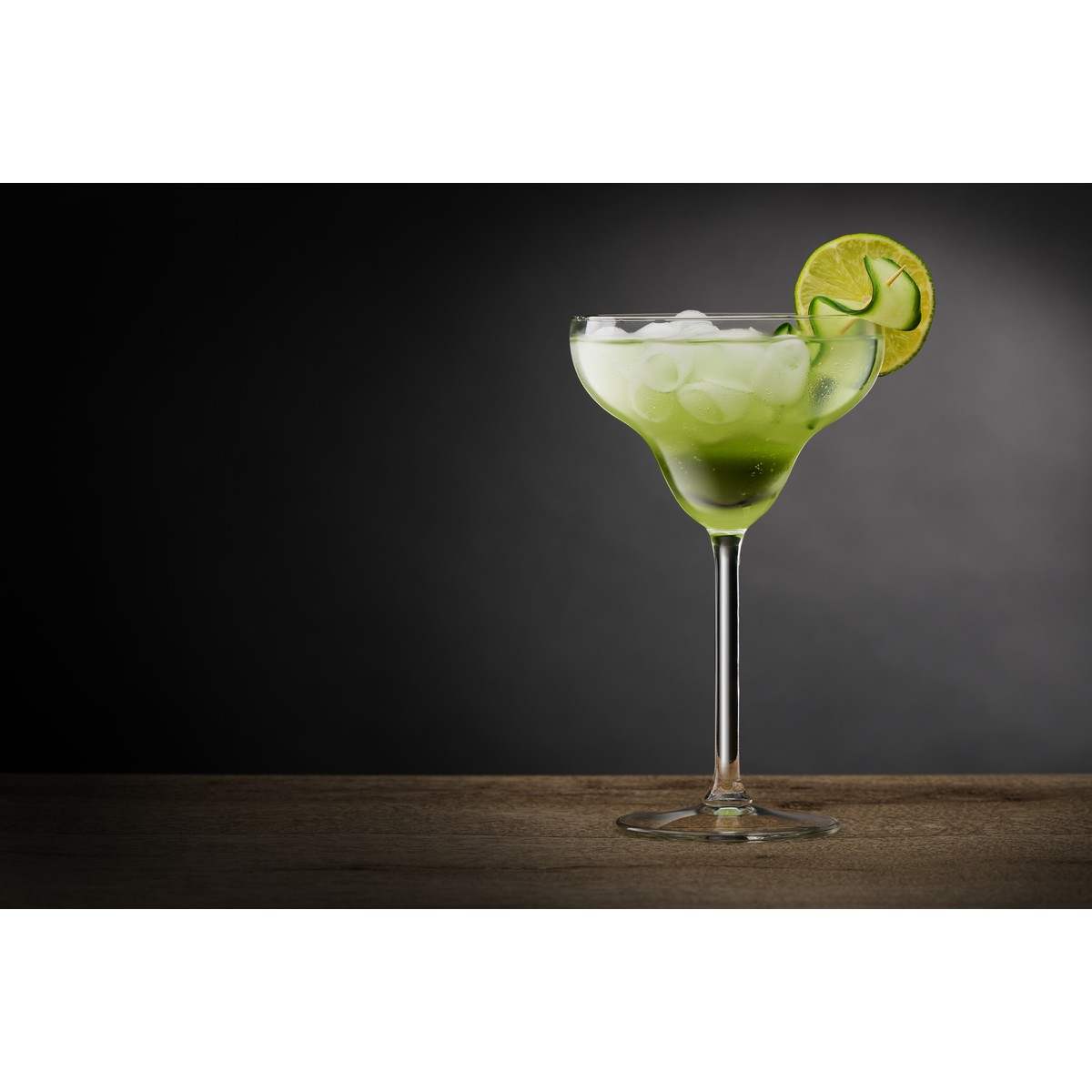 Ein grüner Cocktail mit Eiswürfeln und Limettenscheibe in einem Margarita-Glas.