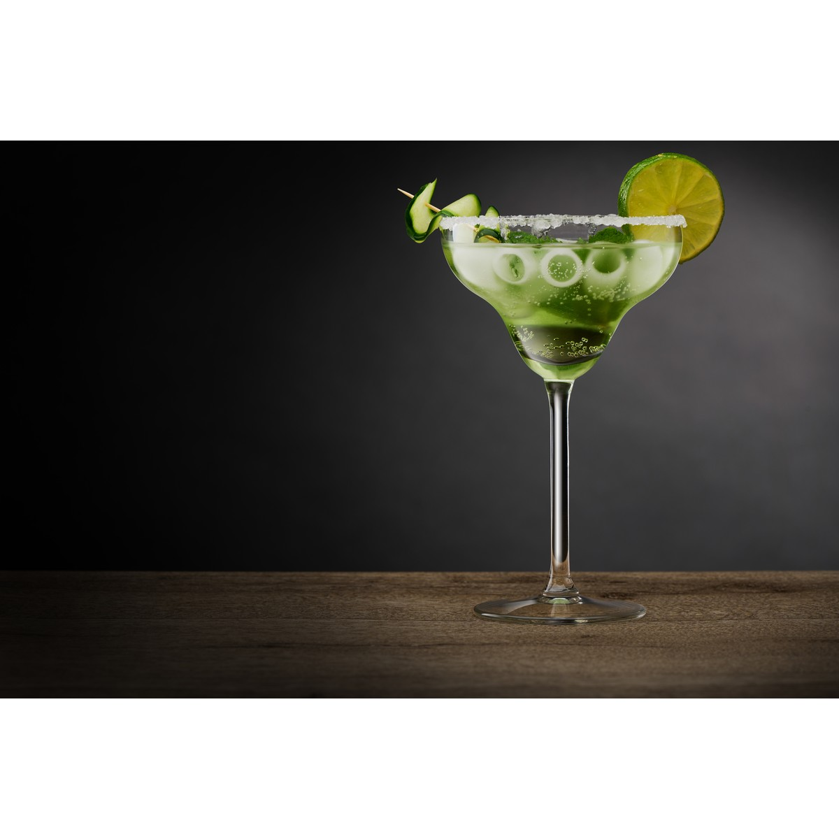 Ein grüner Cocktail in einem Margaritaglas mit Salzrand, Limettenscheibe und Gurkendekoration.