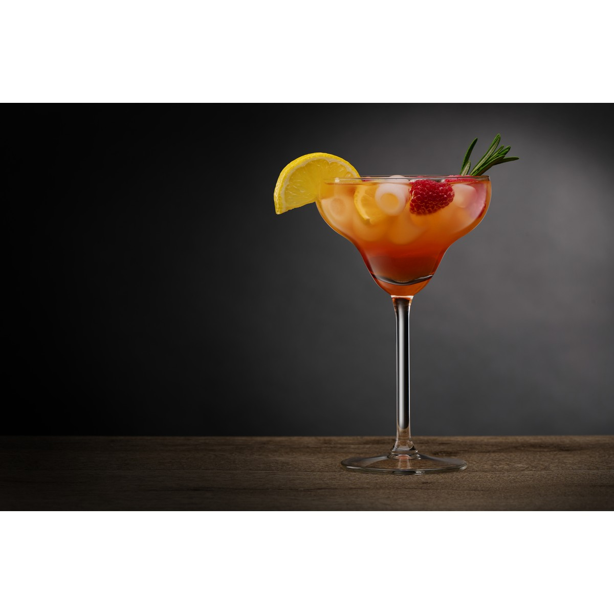 Ein Cocktail mit Eis, Zitrone, Himbeere und Rosmarin auf einem Holztisch.