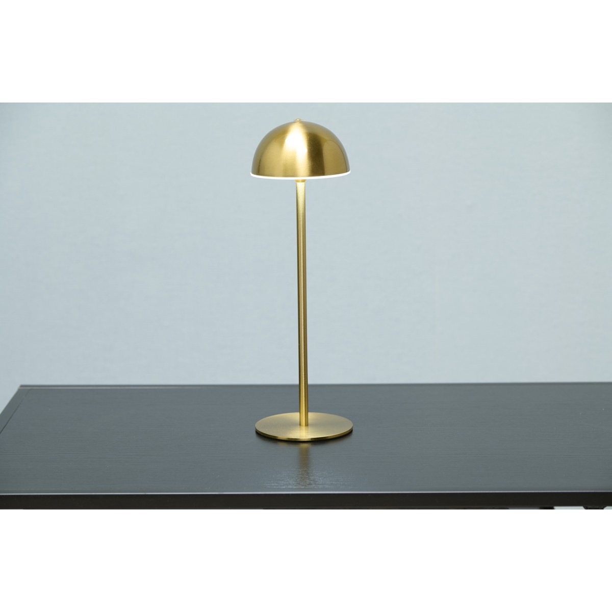 A golden lamp with a rounded shade stands on a dark table.
