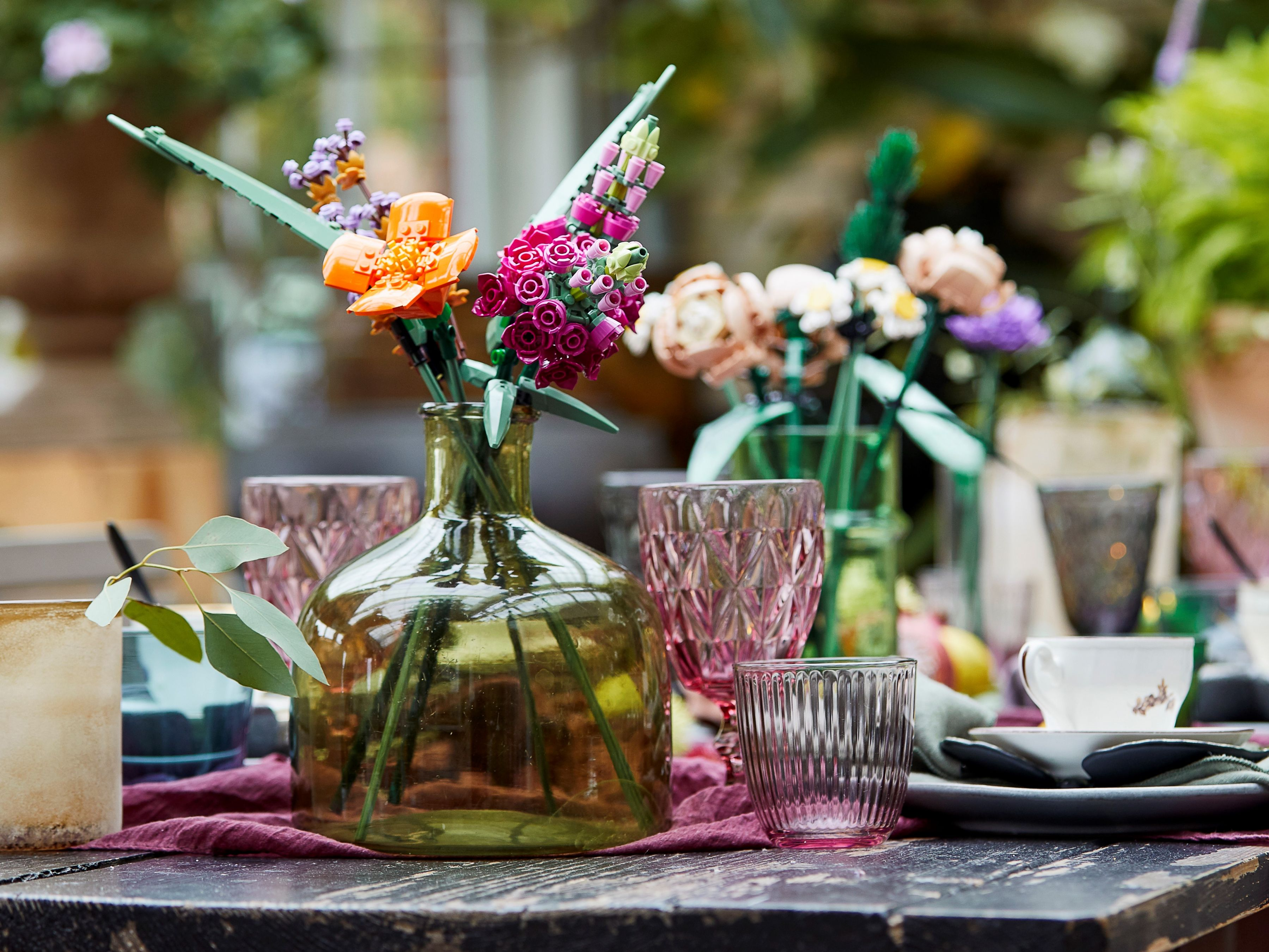 Lego flowers in a vase on a table with glasses and dishes.