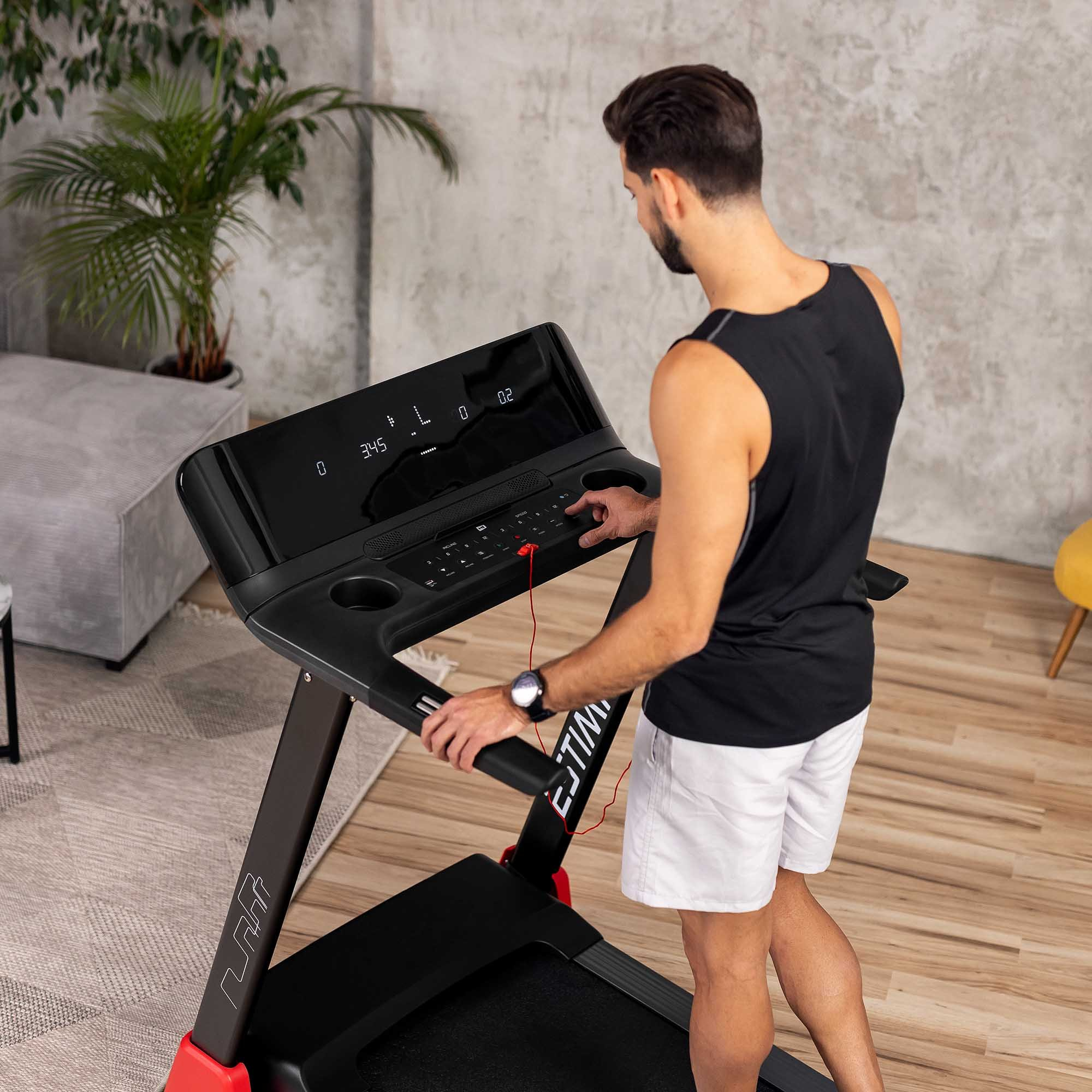 Ein Mann in einem schwarzen Tanktop und weißen Shorts benutzt ein Laufband.