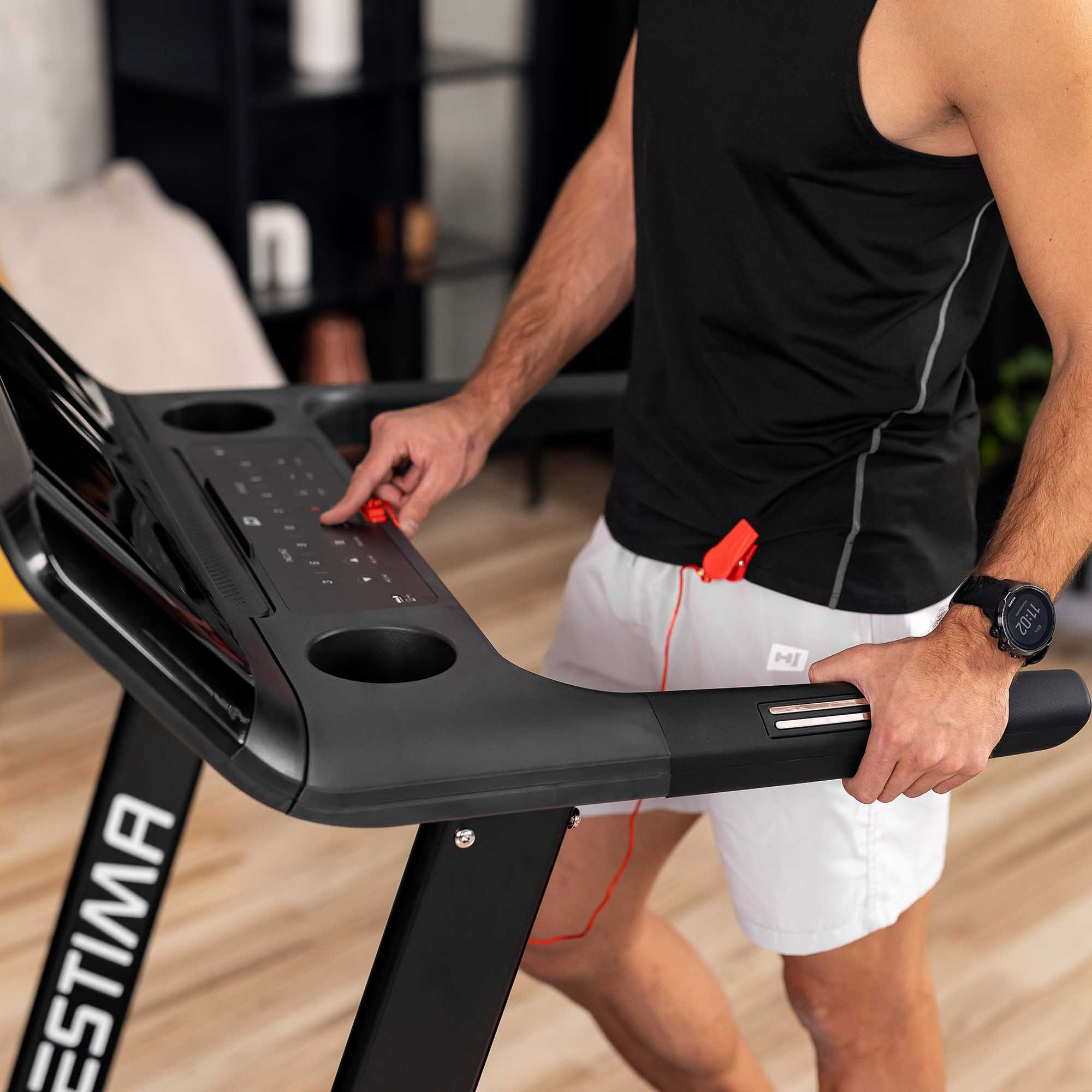 Mann in schwarzem Tanktop und weißen Shorts benutzt ein Laufband.
