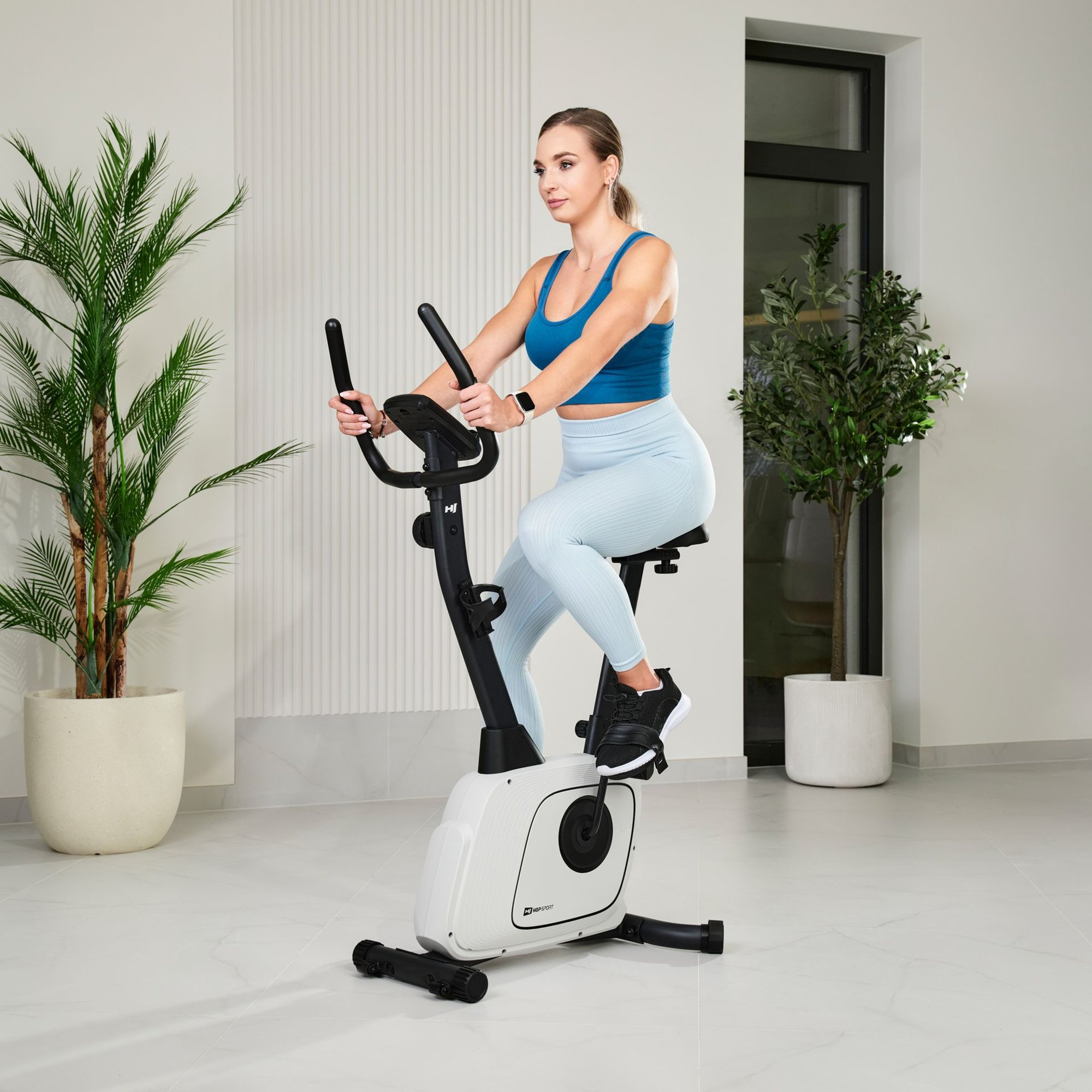 Frau auf einem Heimtrainer in einem blauen Top und hellblauen Leggings.