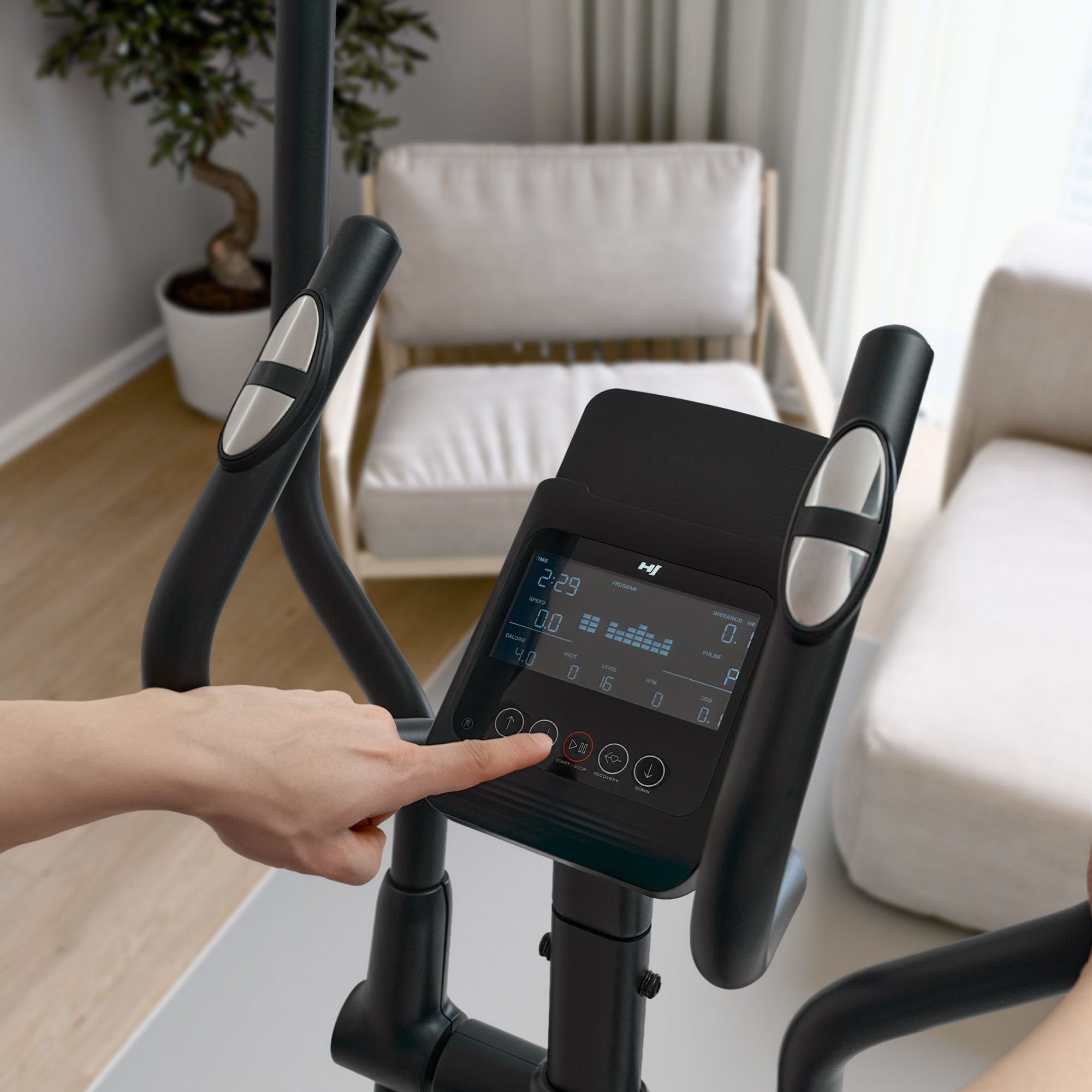 Eine Hand drückt die Start/Stopp-Taste auf dem Display eines Heimtrainers.