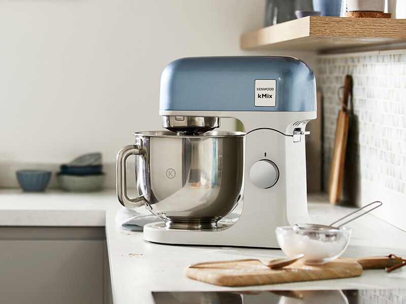 Ein blauer und weißer Küchenmixer steht auf einer Arbeitsplatte mit Schüssel und Schneebesen.