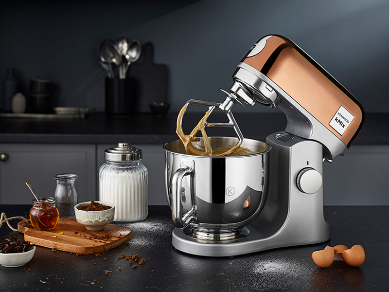 Ein Kupfer-Küchenmaschinen-Mixer mit Teig im Edelstahldom, daneben Zutaten.