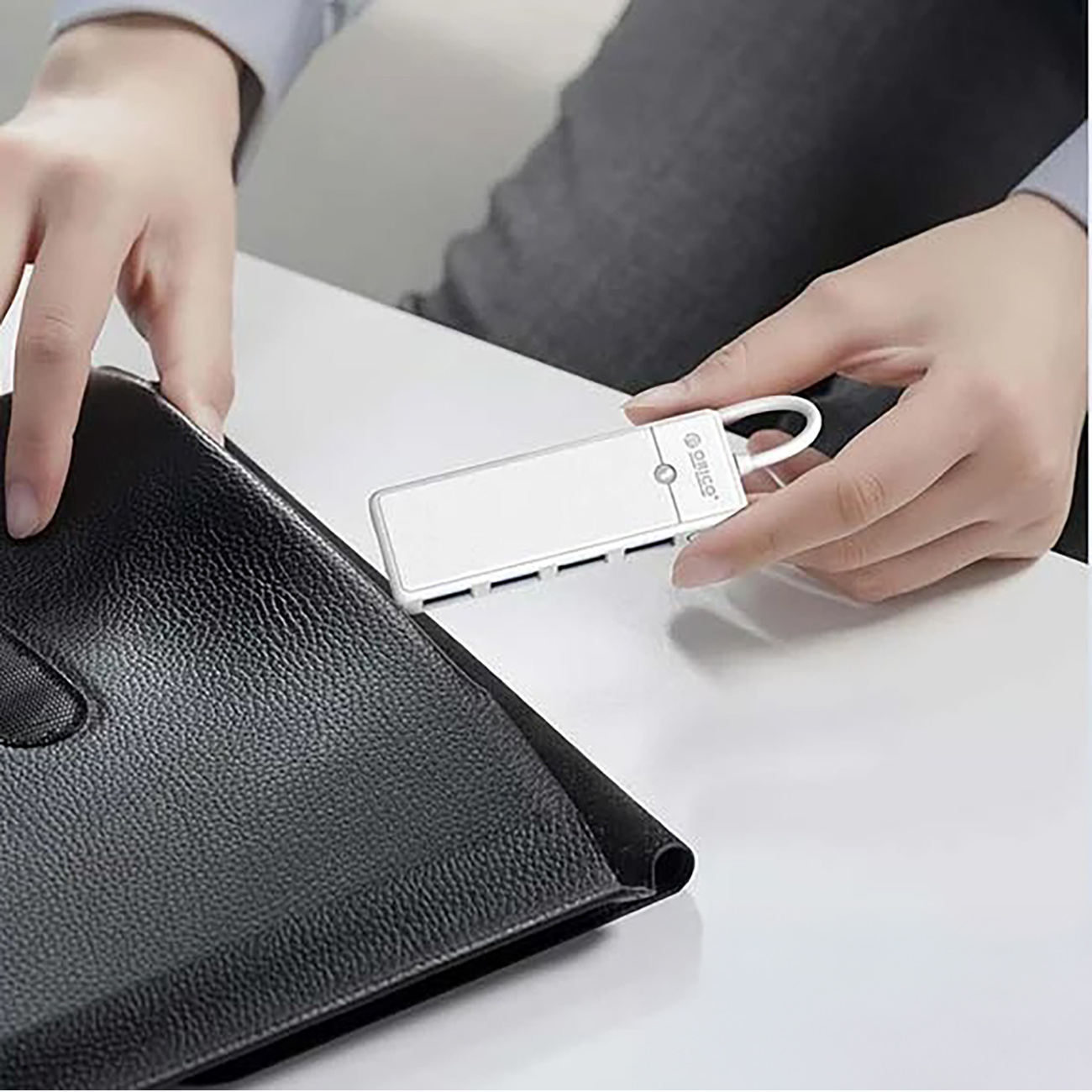 Biały hub USB jest trzymany obok czarnej teczki.