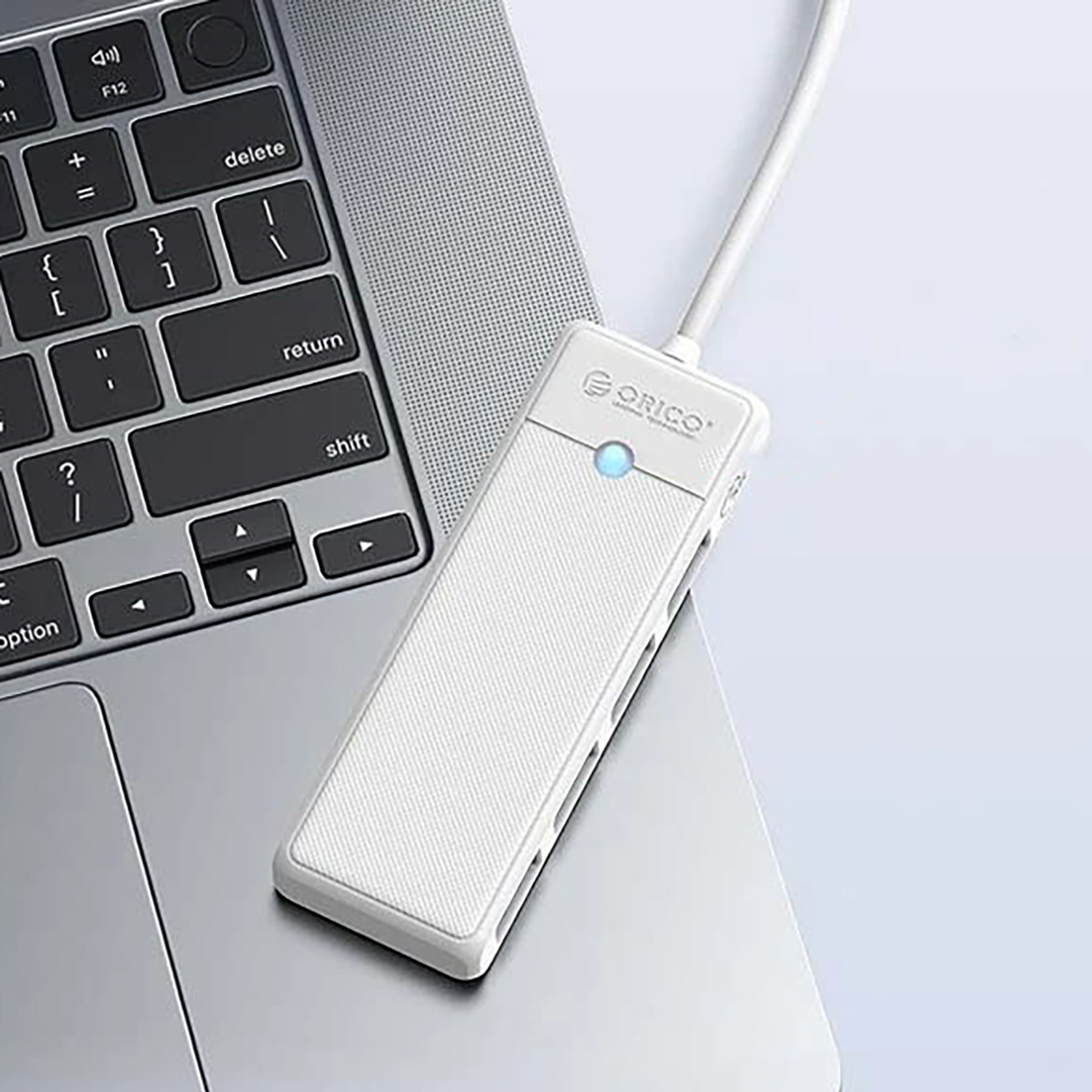 Biały hub USB ORICO z niebieskim światłem na klawiaturze laptopa.