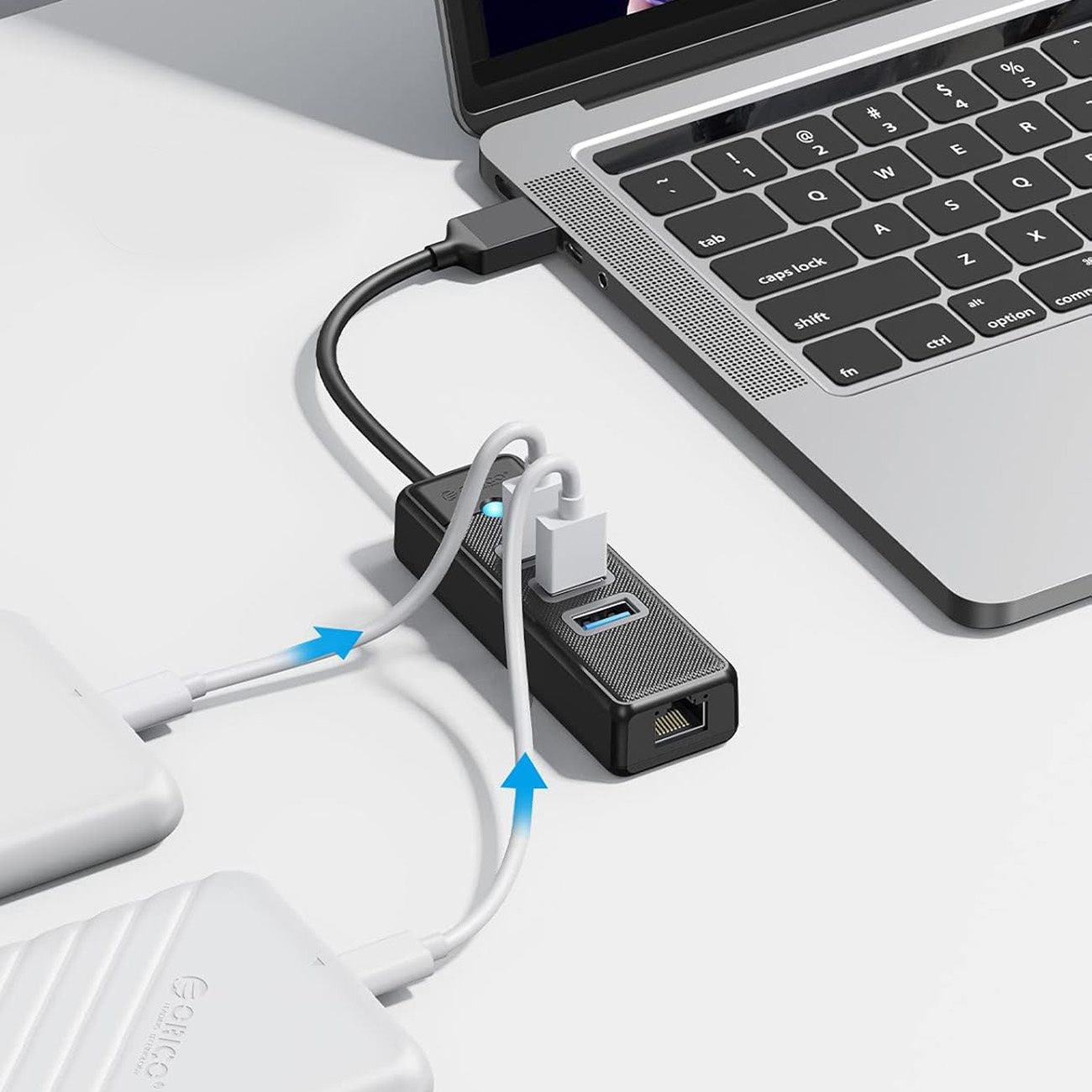Czarny koncentrator USB jest podłączony do laptopa. Dwa białe kable łączą go z urządzeniami zewnętrznymi.