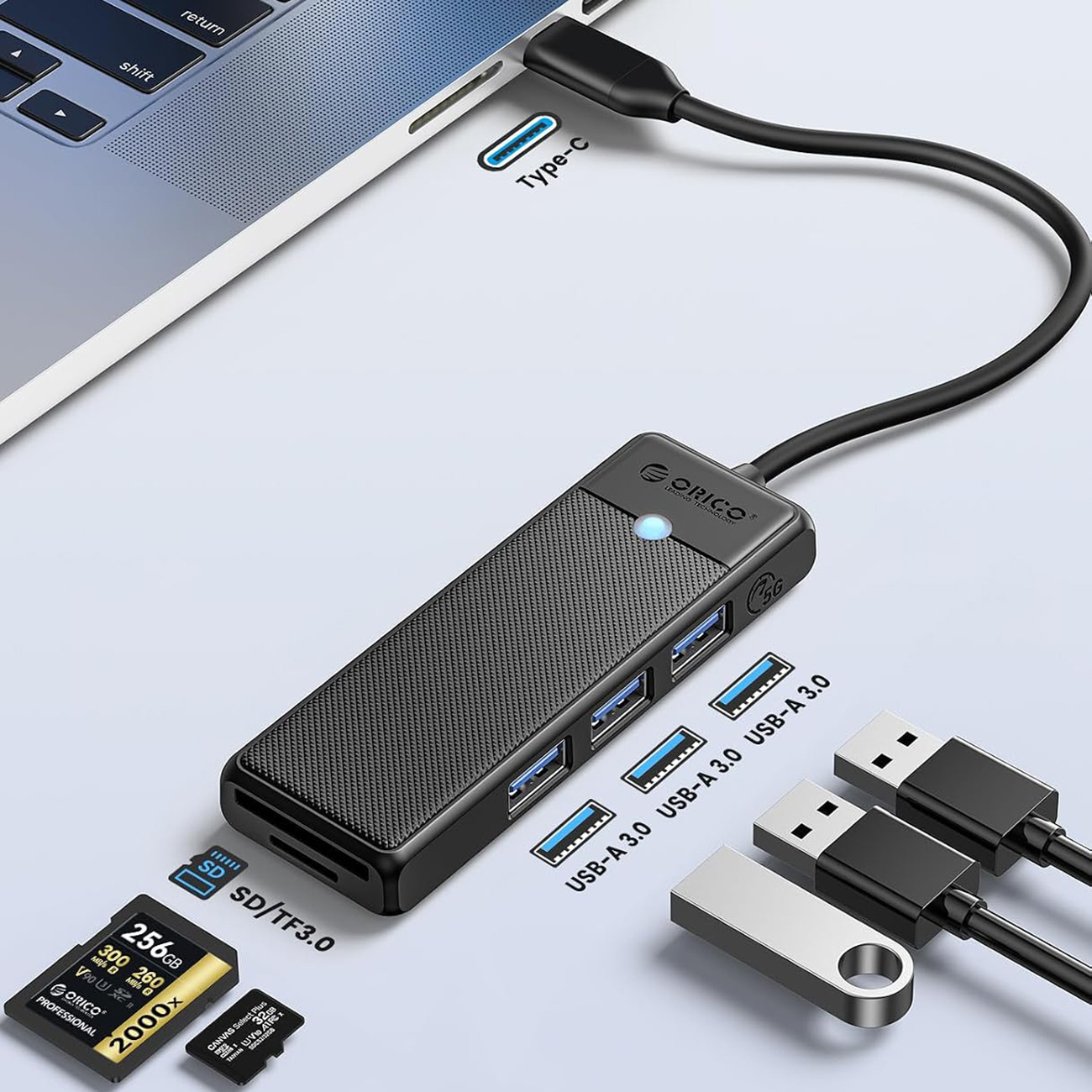 Czarny hub USB-C z czytnikiem kart SD/TF, 4 portami USB-A 3.0, obok laptopa i kart pamięci.