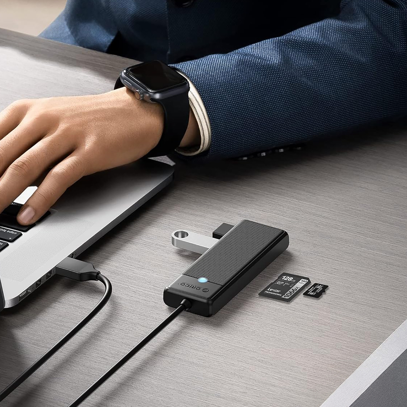 Mężczyzna z zegarkiem smartwatch pisze na laptopie, obok hub USB i karty pamięci.